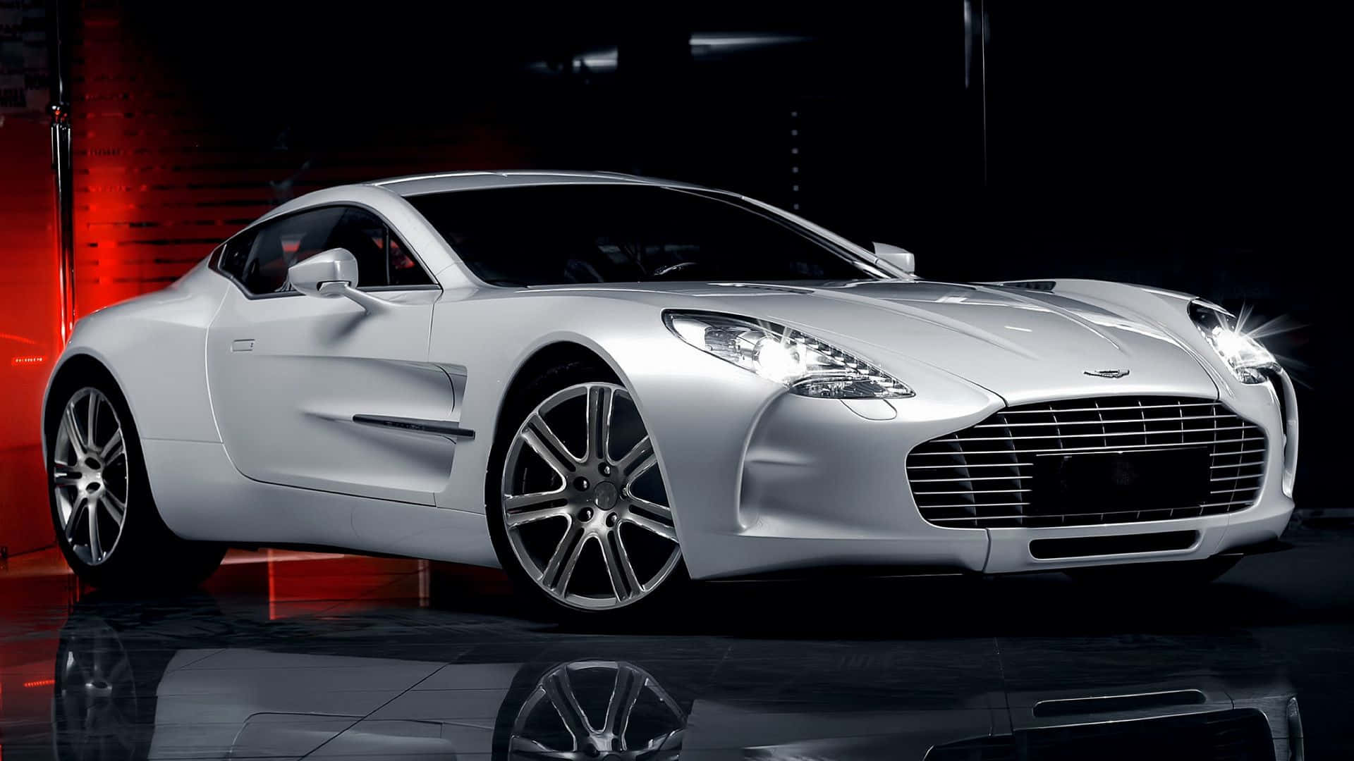 Aston Martin One-77 桌布 壁紙 — 一架時尚的銀色Aston Martin跑車在光亮的攝影棚中，於戲劇性的紅黑燈光下閃閃發光。