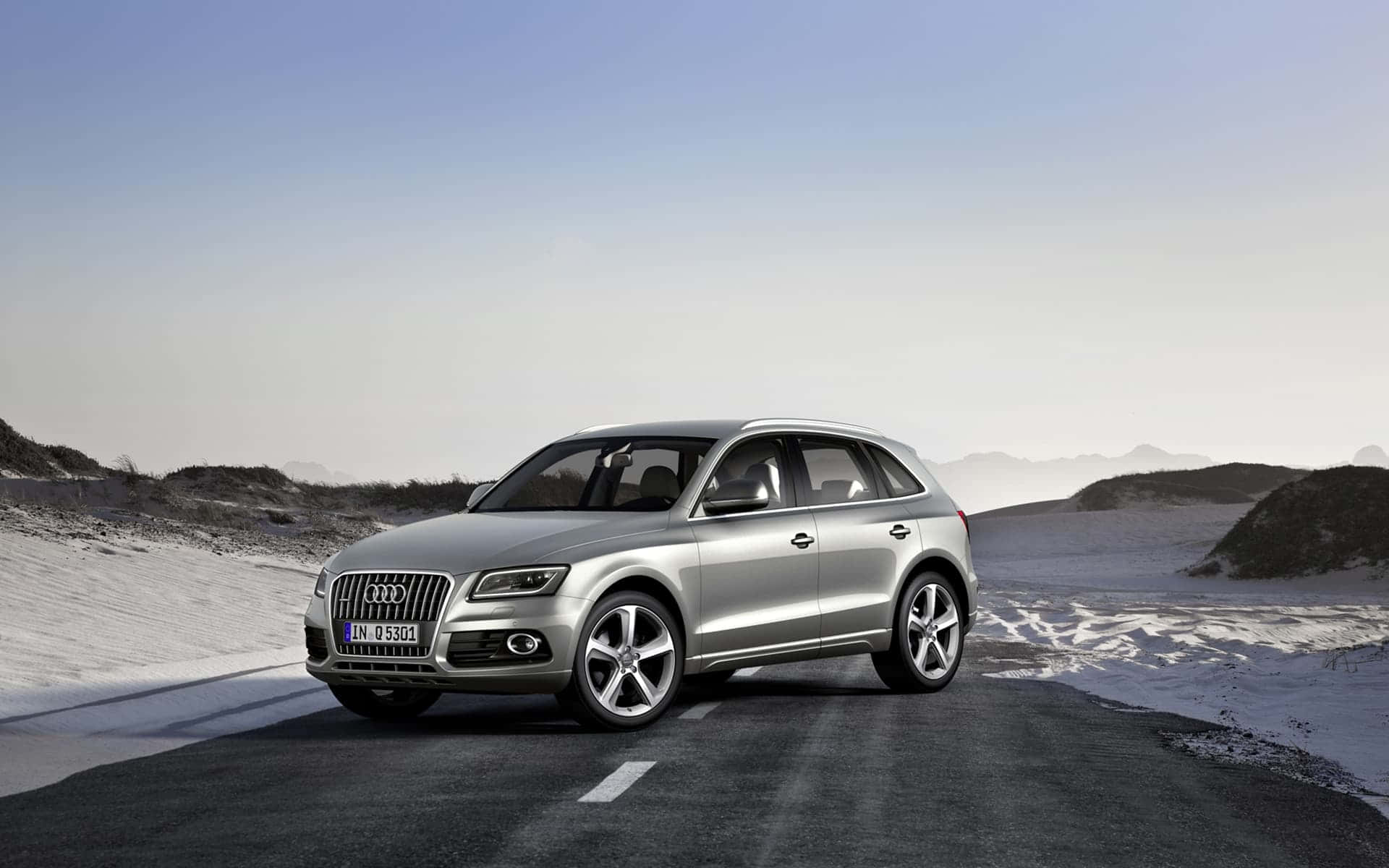 Audi Q5 桌布 壁紙 — 一輛時尚的銀色奧迪Q5 SUV在晴朗藍天下，行駛於白雪覆蓋的山區蜿蜒道路上。