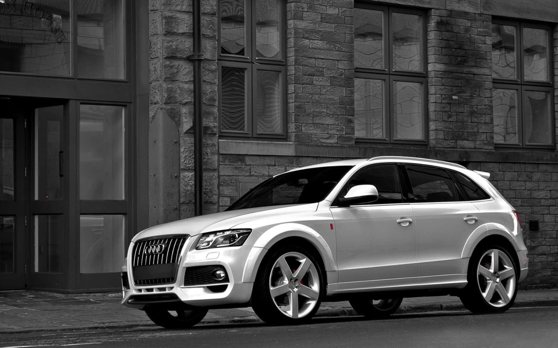 Audi Q5 桌布 壁紙 — 一輛時尚的銀色Audi Q7 SUV停放在城市街道旁的石造建築物旁，以單色呈現。