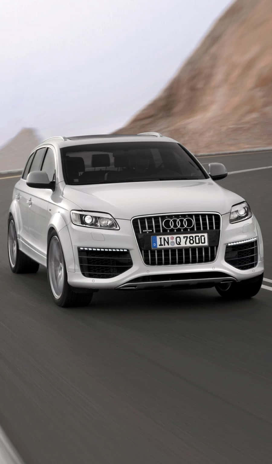 Audi Q7 桌布 壁紙 — 一輛時尚的銀色Audi Q7 SUV沿著蜿蜒的山路疾馳，背景是模糊的動感和岩石地形。