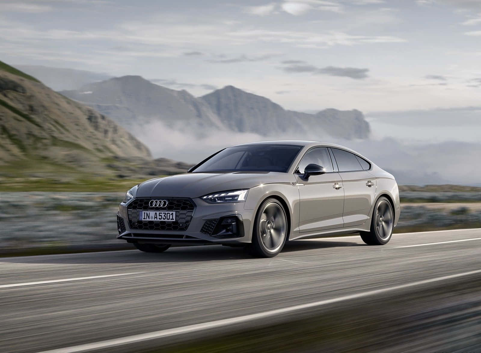 Audi A5 桌布 壁紙 — 一輛時尚的銀色奧迪轎車沿著山路疾馳，背景是霧氣繚繞的山峰和陰雲密佈的天空。