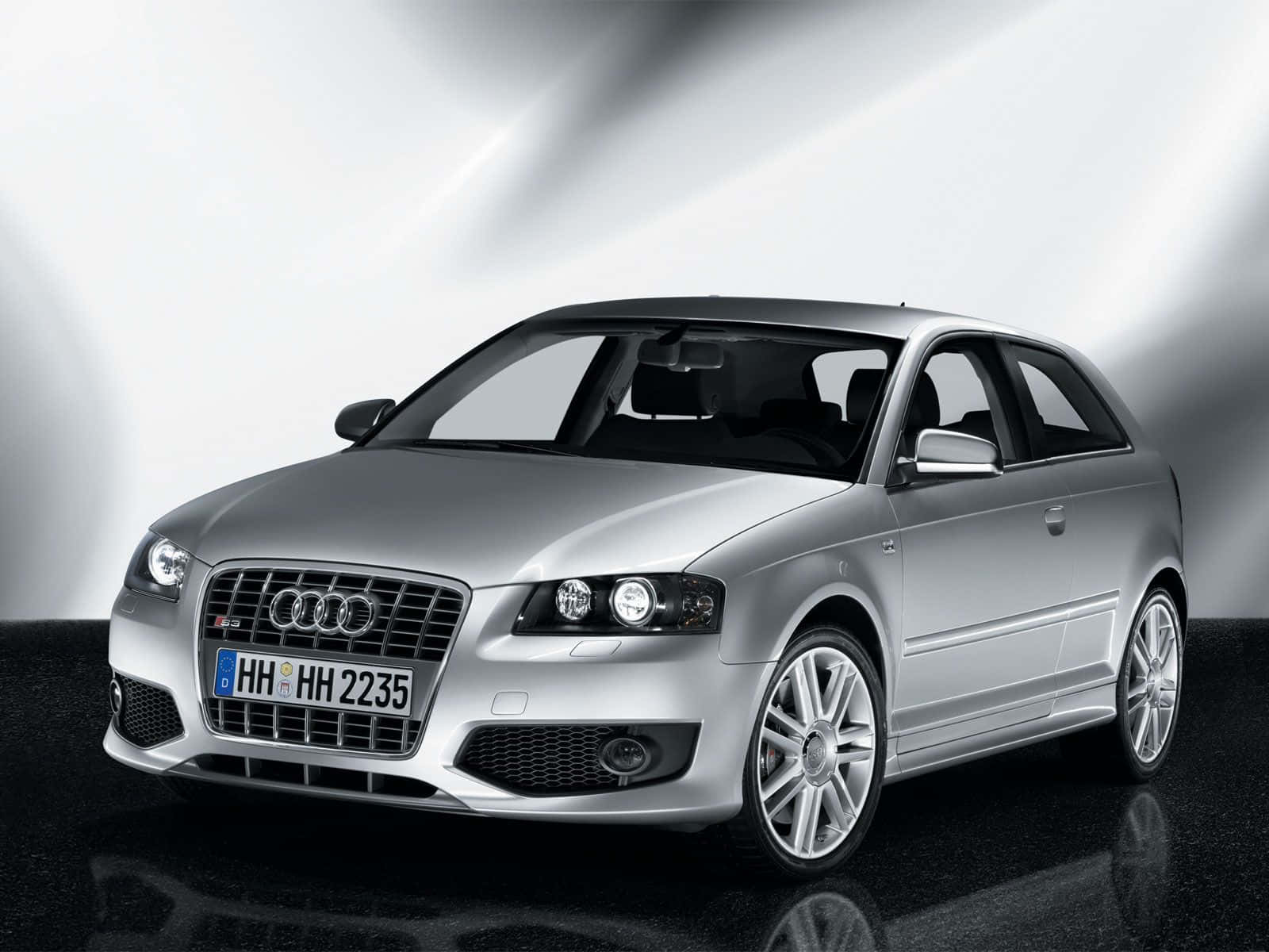 Audi S3 桌布 壁紙 — 一輛配備合金輪圈的時尚銀色奧迪跑車在燈光效果強烈、地板反光的攝影棚中展示。