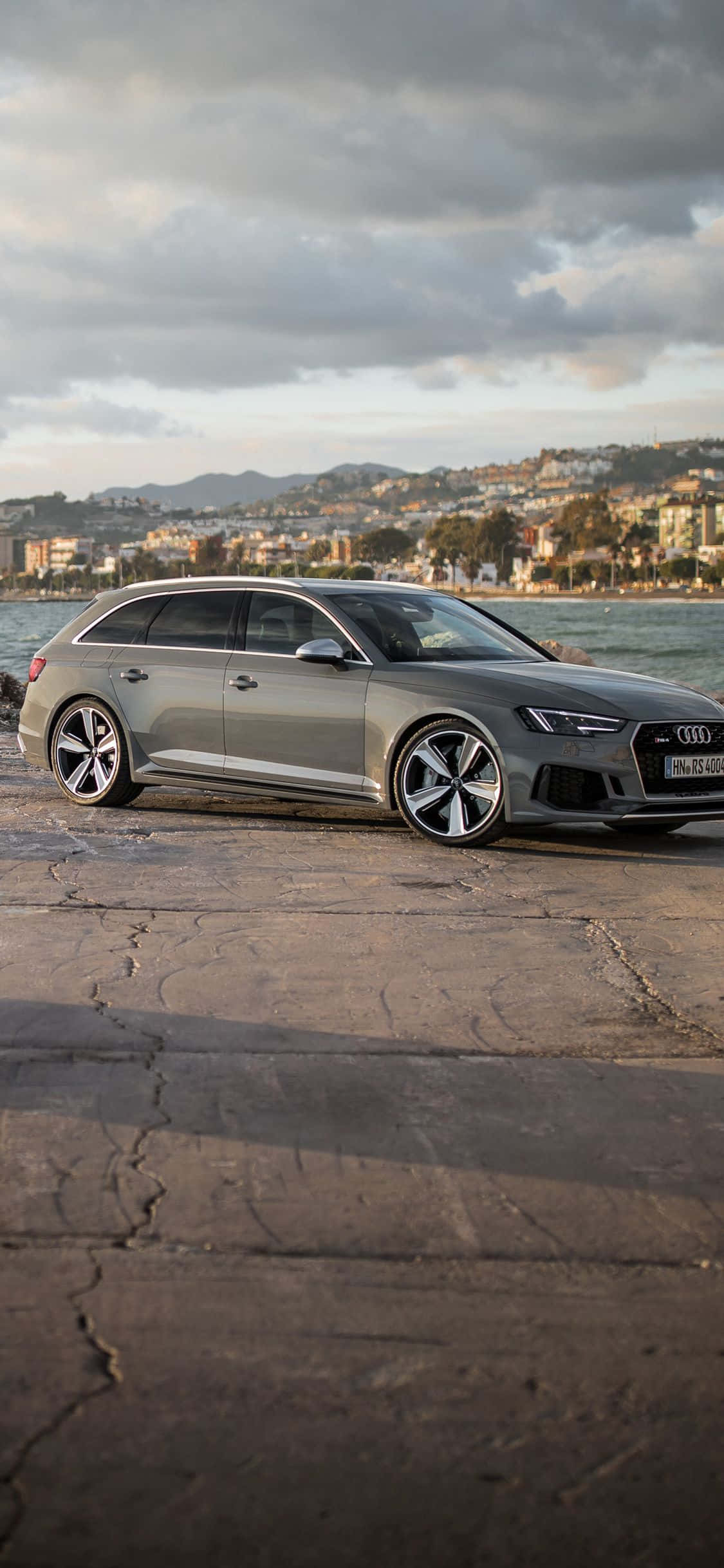 Audi Rs5 桌布 壁紙 — 一輛時尚的銀色 Audi 旅行車停泊在海邊裂開的混凝土上，天空多雲。