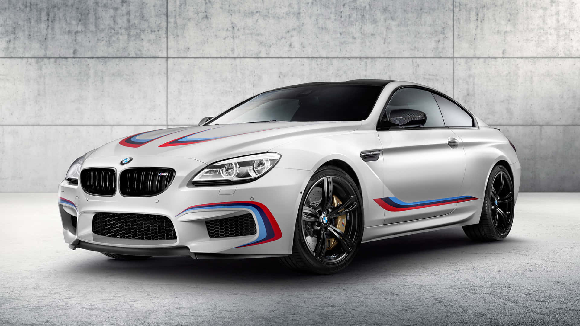Bmw M6 桌布 壁紙 — 一架時尚的銀色寶馬M6雙門跑車，帶有醒目的藍、紅、白賽車條紋，在極簡混凝土背景下蓄勢待發。