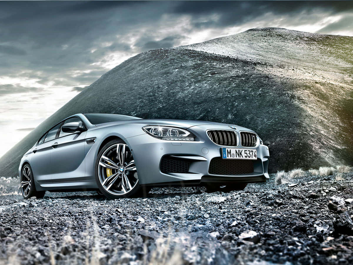 Bmw M6 桌布 壁紙 — 一架流線型銀色BMW M6跑車停放在岩石地形上，背後有巨大的黑暗山丘，天空風暴密佈。