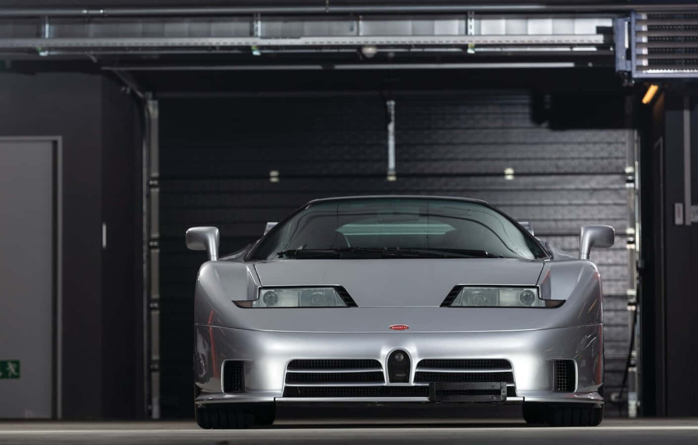 Bugatti Eb110 桌布 壁紙 — 一架流線型銀色Bugatti EB110 Super Sport停放在昏暗的工業車庫中，頭頂有裸露的金屬橫樑。