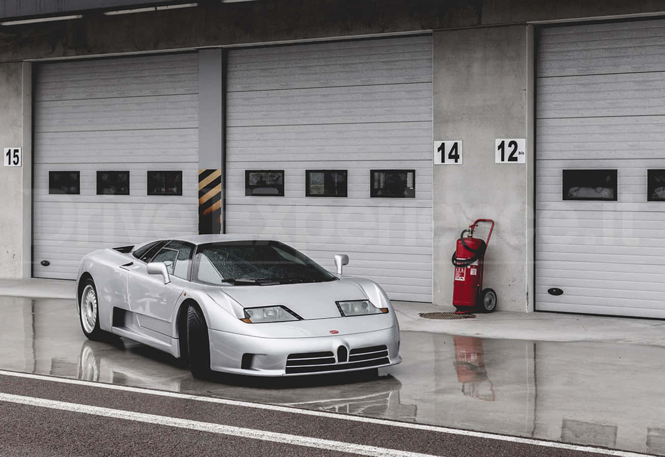 Bugatti Eb110 桌布 壁紙 — 一輛時尚的銀色Bugatti跑車在潮濕的混凝土地板上閃閃發光，前面是帶有編號的工業車庫門。