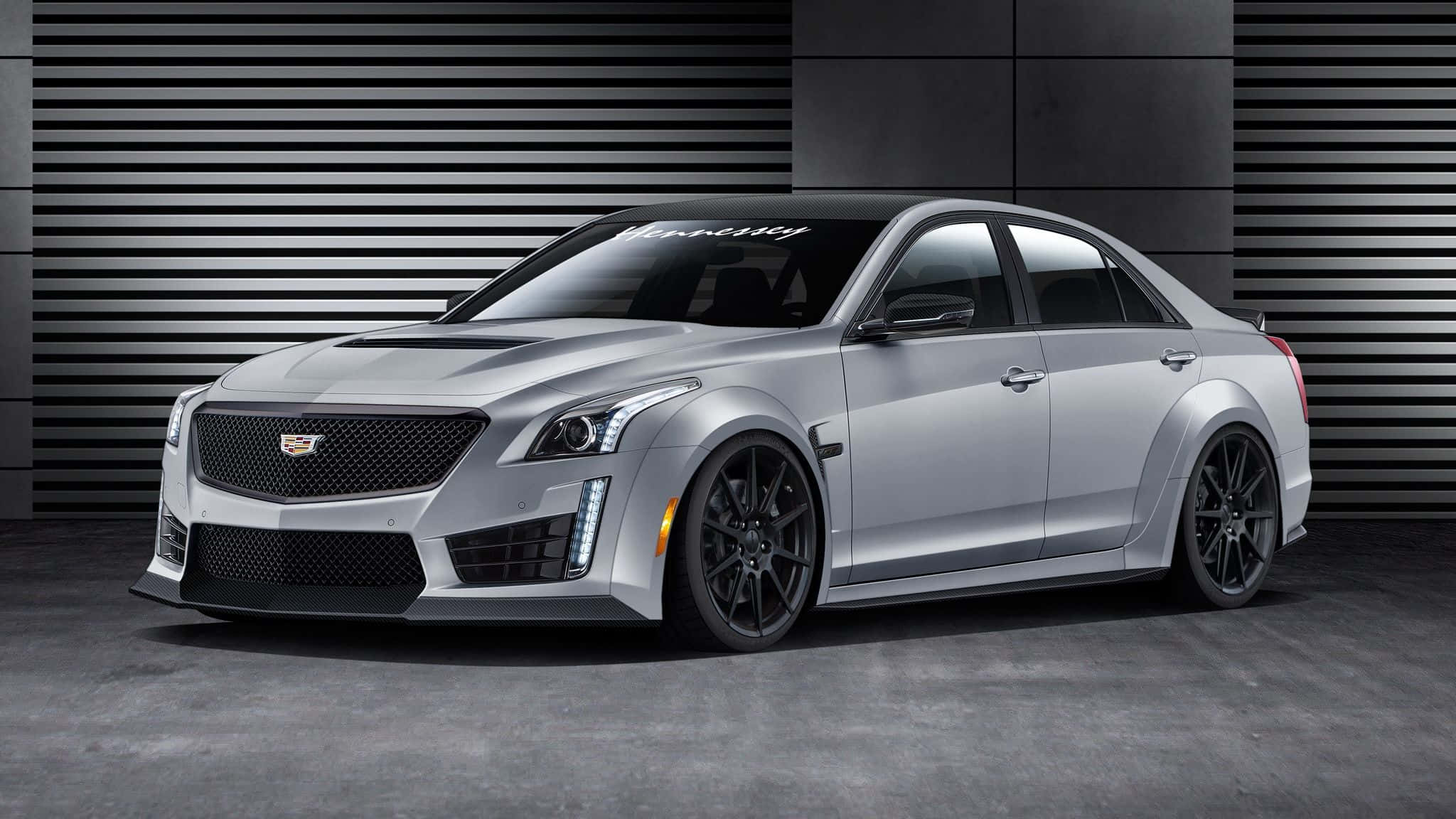 Cadillac Cts 桌布 壁紙 — 一輛時尚的銀色Cadillac CTS-V運動轎車，帶有黑色飾件和定制輪圈，在現代工業背景下蓄勢待發。