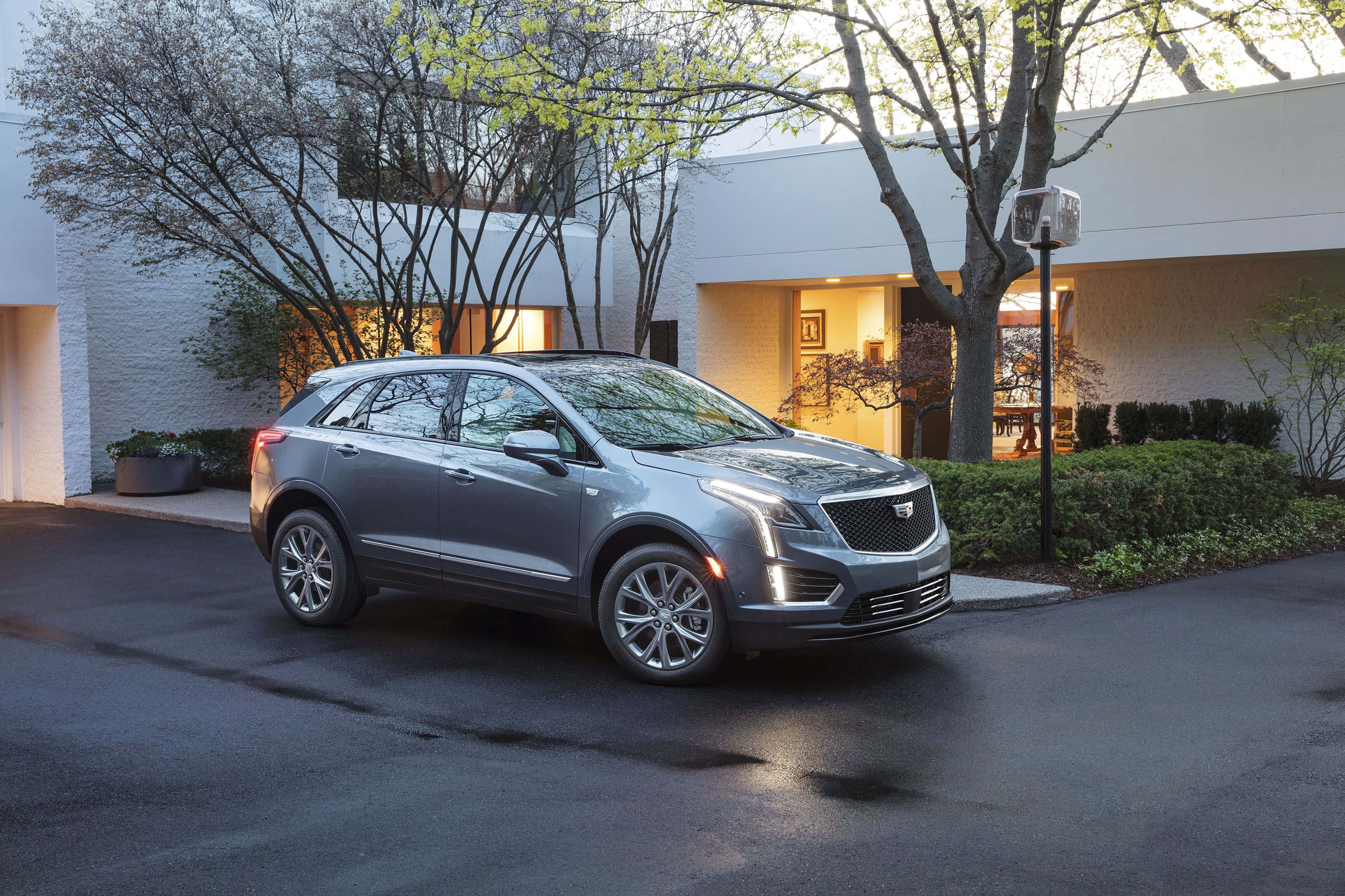 Cadillac Xt5 桌布 壁紙 — 一輛時尚的銀色Cadillac SUV在黃昏時停放在現代白色房屋前的濕車道上。