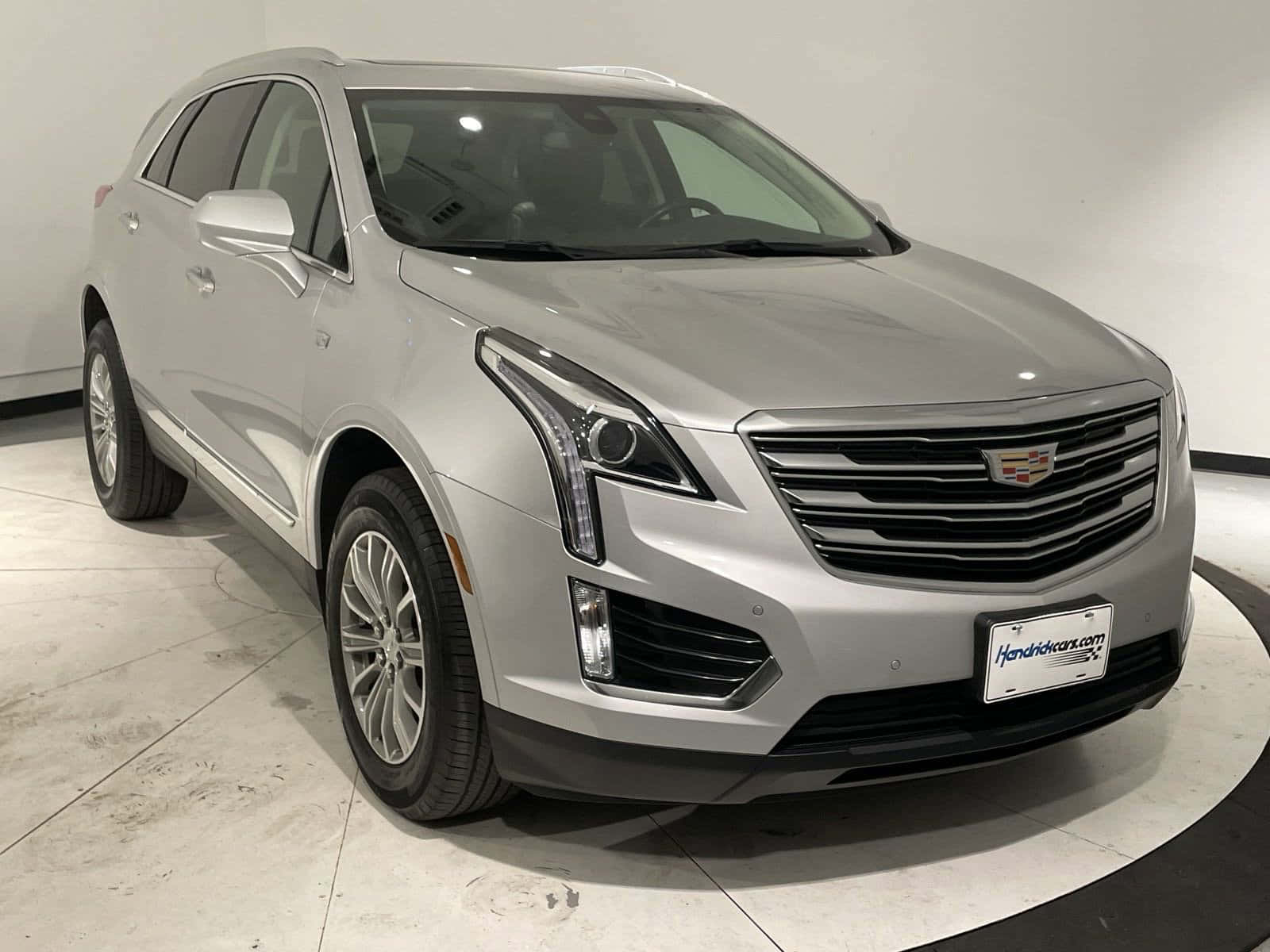 Cadillac Xt5 桌布 壁紙 — 一輛時尚的銀色Cadillac XT5 SUV在明亮的室內展廳中展示，地板為拋光混凝土。