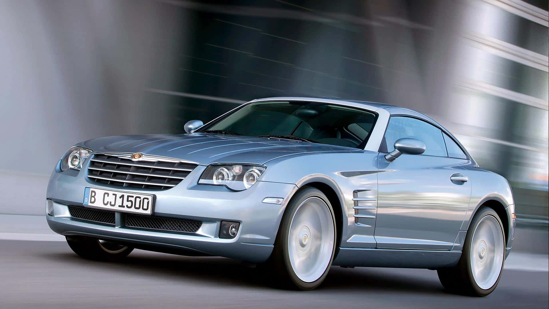 Chrysler Crossfire 桌布 壁紙 — 一輛時尚的銀色 Chrysler Crossfire 跑車在現代玻璃建築背景下高速駛過，帶有動態模糊效果。