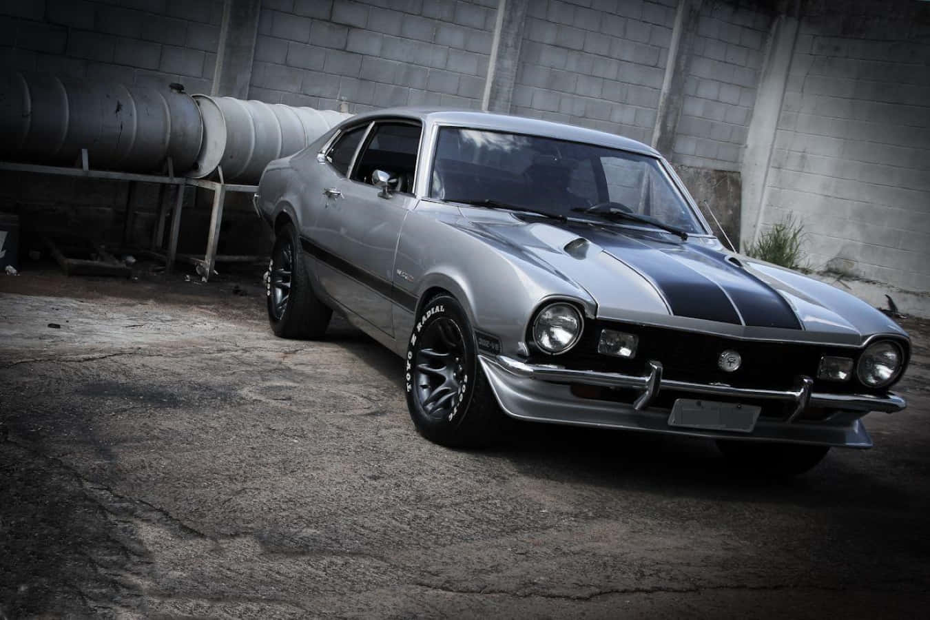 Ford Maverick 桌布 壁紙 — 一輛流線型銀色經典肌肉車，帶有黑色賽車條紋，停放在粗獷的工業倉庫中。