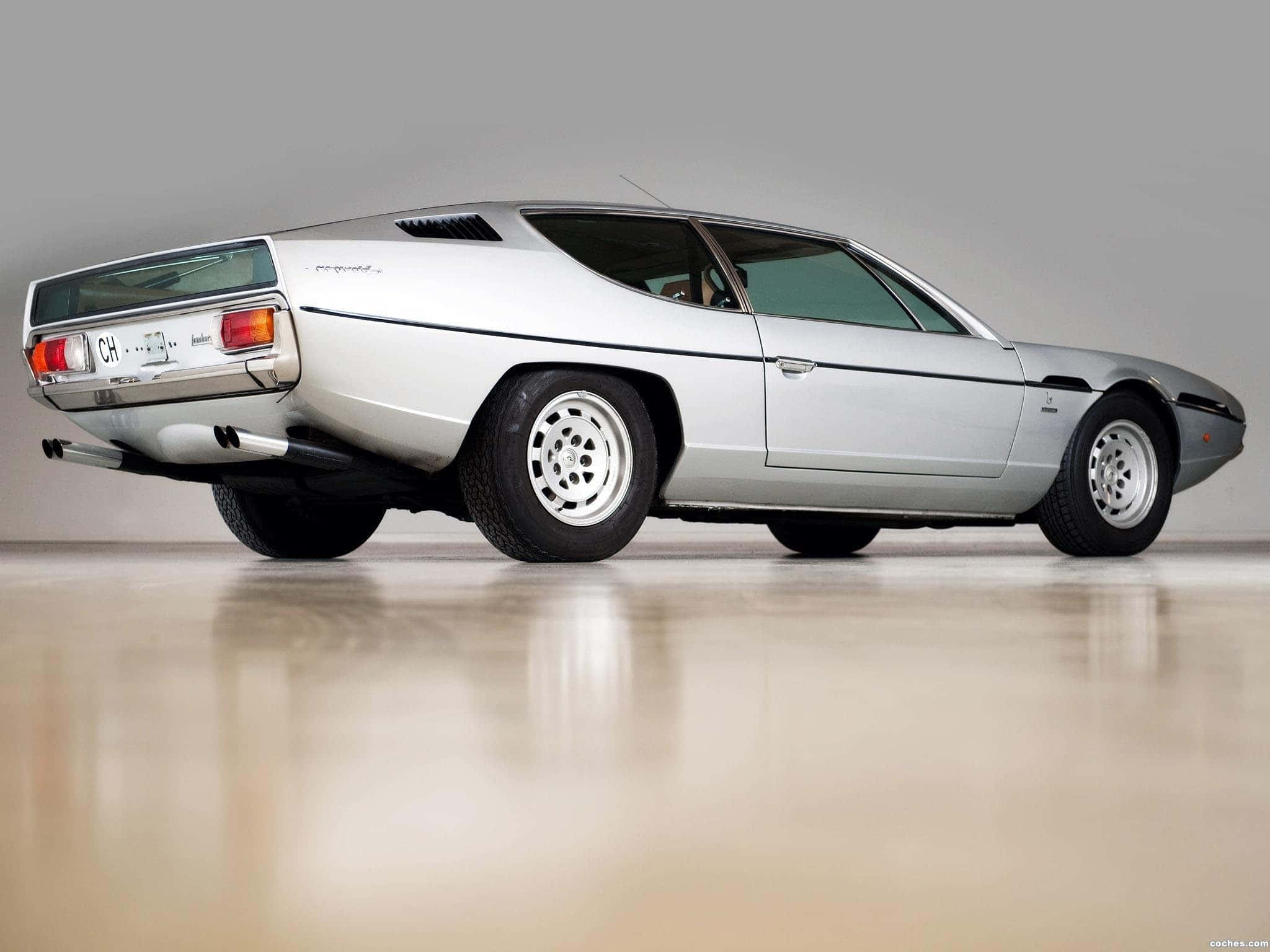 Lamborghini Espada 桌布 壁紙 — 一輛線條流暢的銀色經典跑車，具有低矮車身和獨特的尾部設計，在極簡風格的攝影棚中展示。