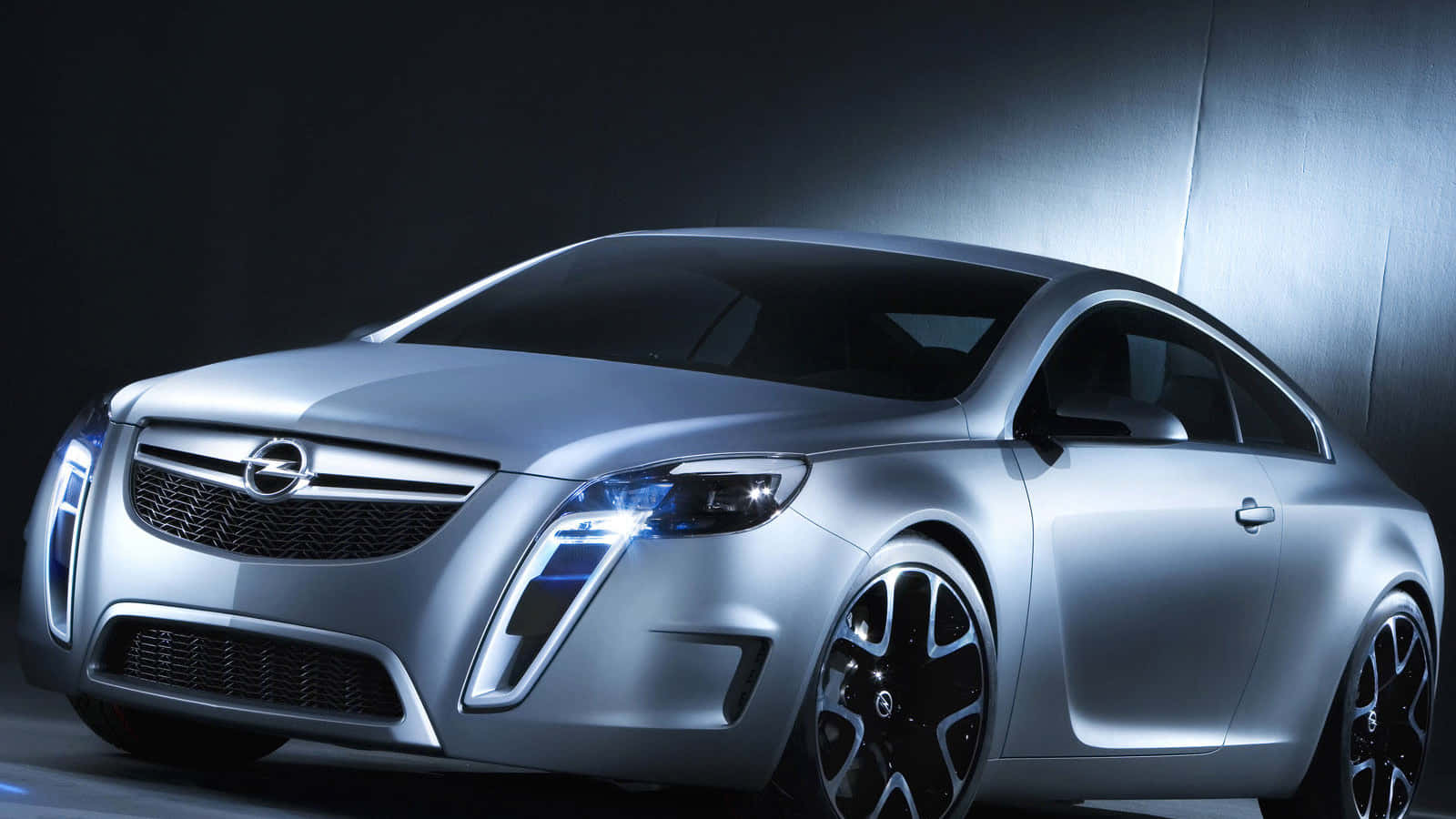 Opel Vectra 桌布 壁紙 — 一輛時尚的銀色概念車，配備發光的藍色車頭燈，在戲劇性的工作室燈光下，以深色紋理牆壁為背景展示。