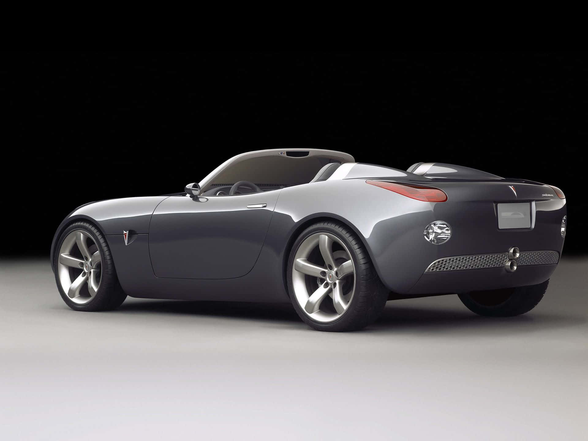 Pontiac Solstice 桌布 壁紙 — 時尚的銀色敞篷跑車，採用極簡設計和紅色尾燈，在黑白工作室背景下展示。
