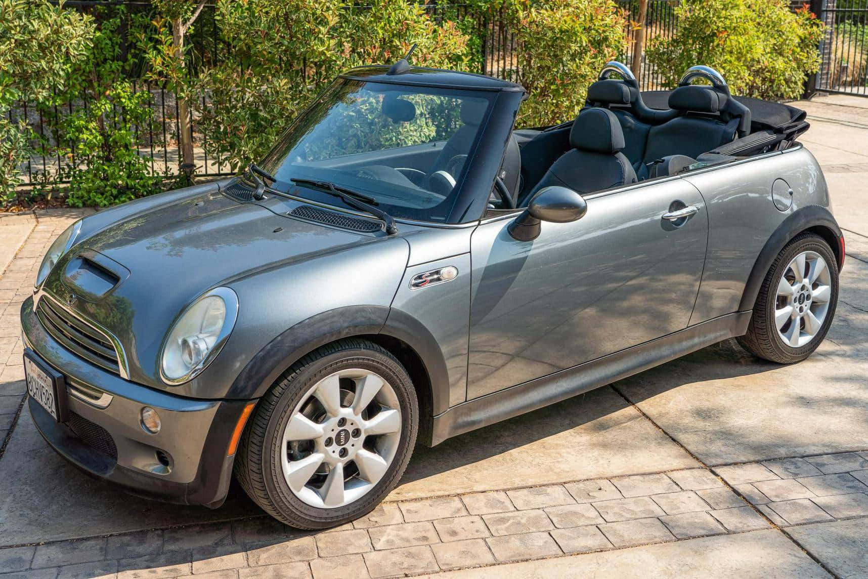 Mini Cooper S Convertible 桌布 壁紙 — 一輛時尚的銀色敞篷跑車停放在陽光普照的石頭車道上，背景是茂密的綠色灌木叢。