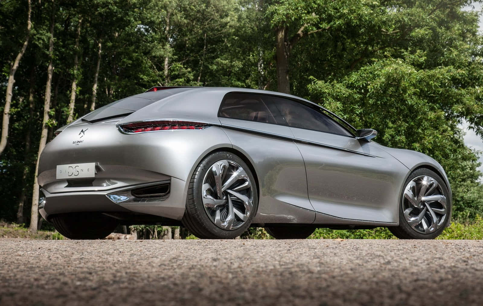 壁紙 — 一輛時尚的銀色 DS E-Tense 概念車停在碎石上，背景是茂密的綠樹。