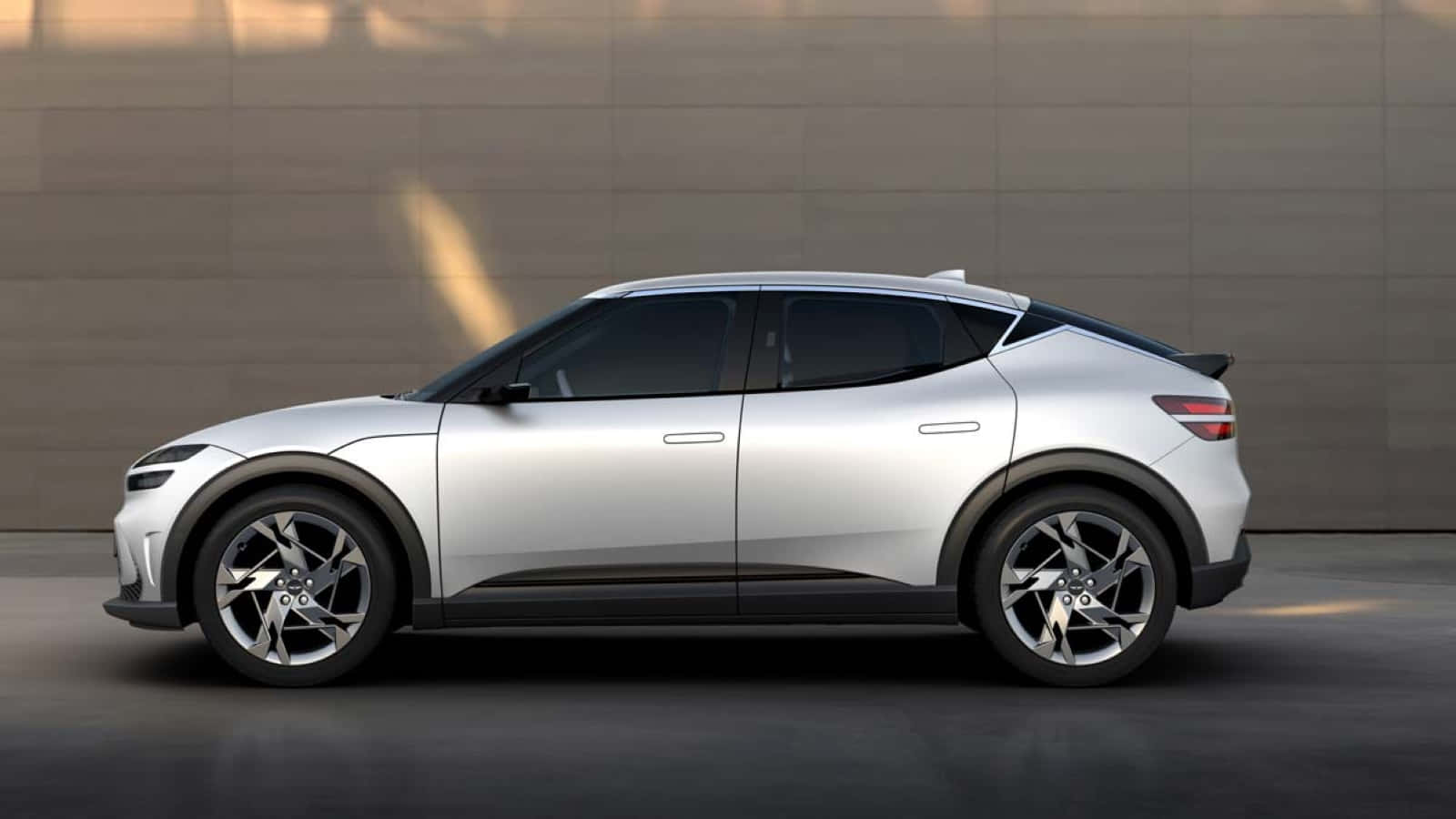 Genesis Gv60 桌布 壁紙 — 一輛時尚的銀色電動SUV以側面輪廓矗立在簡約的混凝土牆前，帶有柔和的金色燈光。