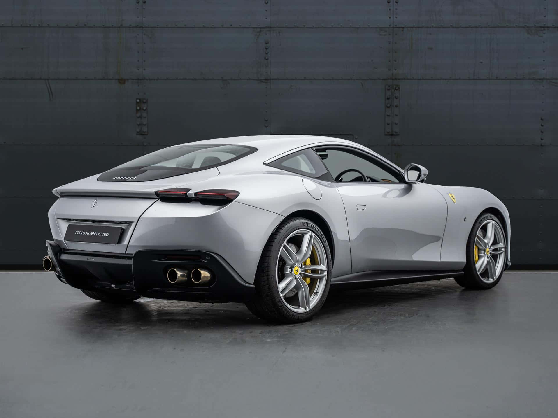 Ferrari Roma 桌布 壁紙 — 一輛時尚的銀色法拉利 Purosangue 轎跑車，從後方四分之三角度展示，背景為深色工業牆。