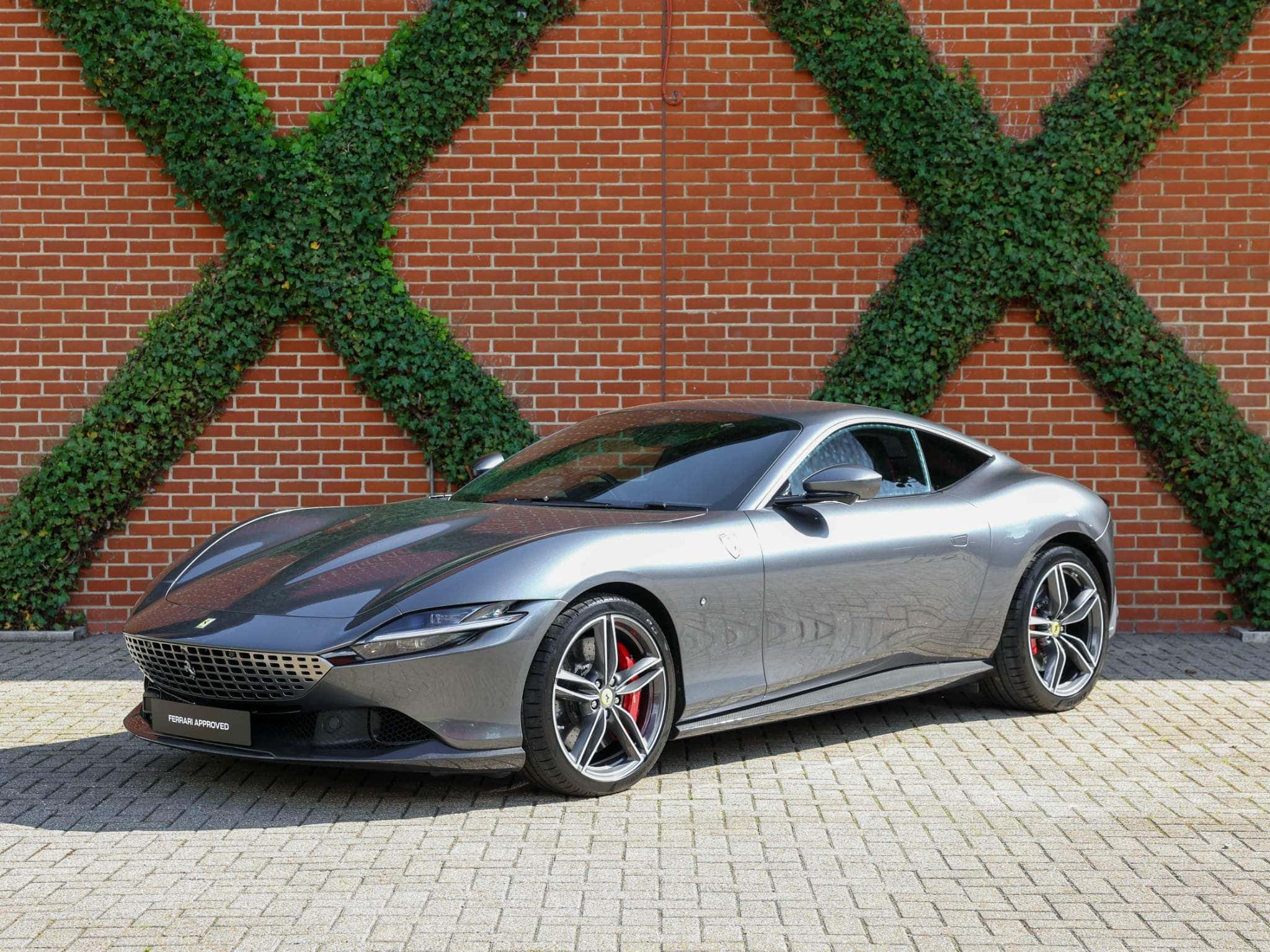 Ferrari Roma 桌布 壁紙 — 一輛時尚的銀色法拉利 Roma 停放在磚砌庭院中，背景是紅磚牆，牆上綠色常春藤形成 X 形。