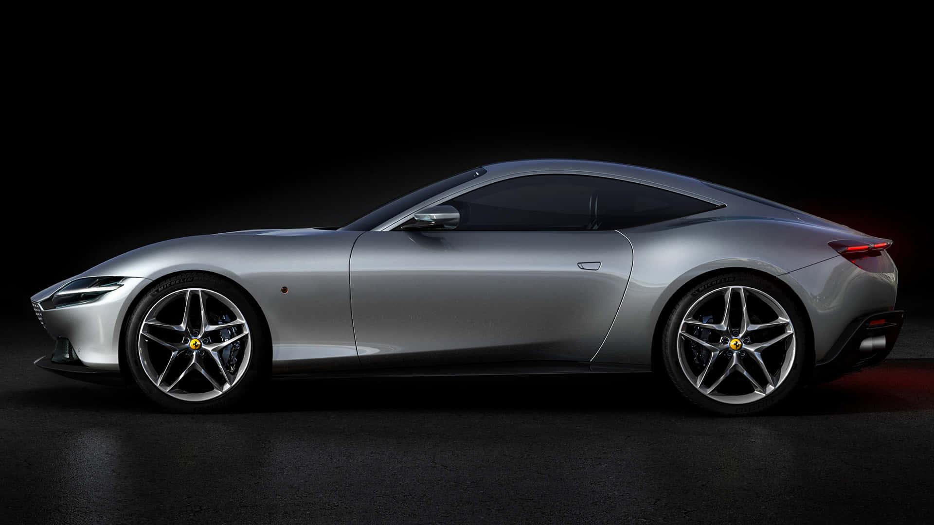 Ferrari Roma 桌布 壁紙 — 一輛時尚的銀色法拉利跑車在簡潔的黑色工作室背景中以側面輪廓滑行，配以戲劇性的燈光。