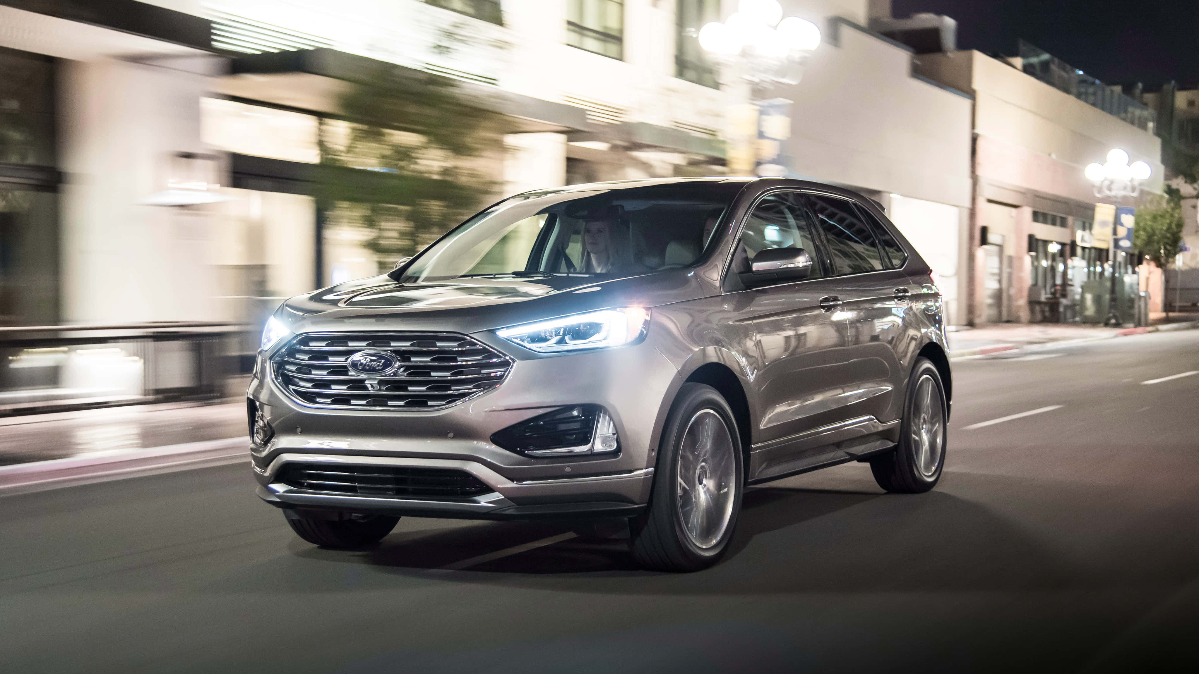 Ford Edge 桌布 壁紙 — 一輛流線型銀色福特Edge SUV在夜間城市街道上飛馳，燈光和建築物模糊移動。