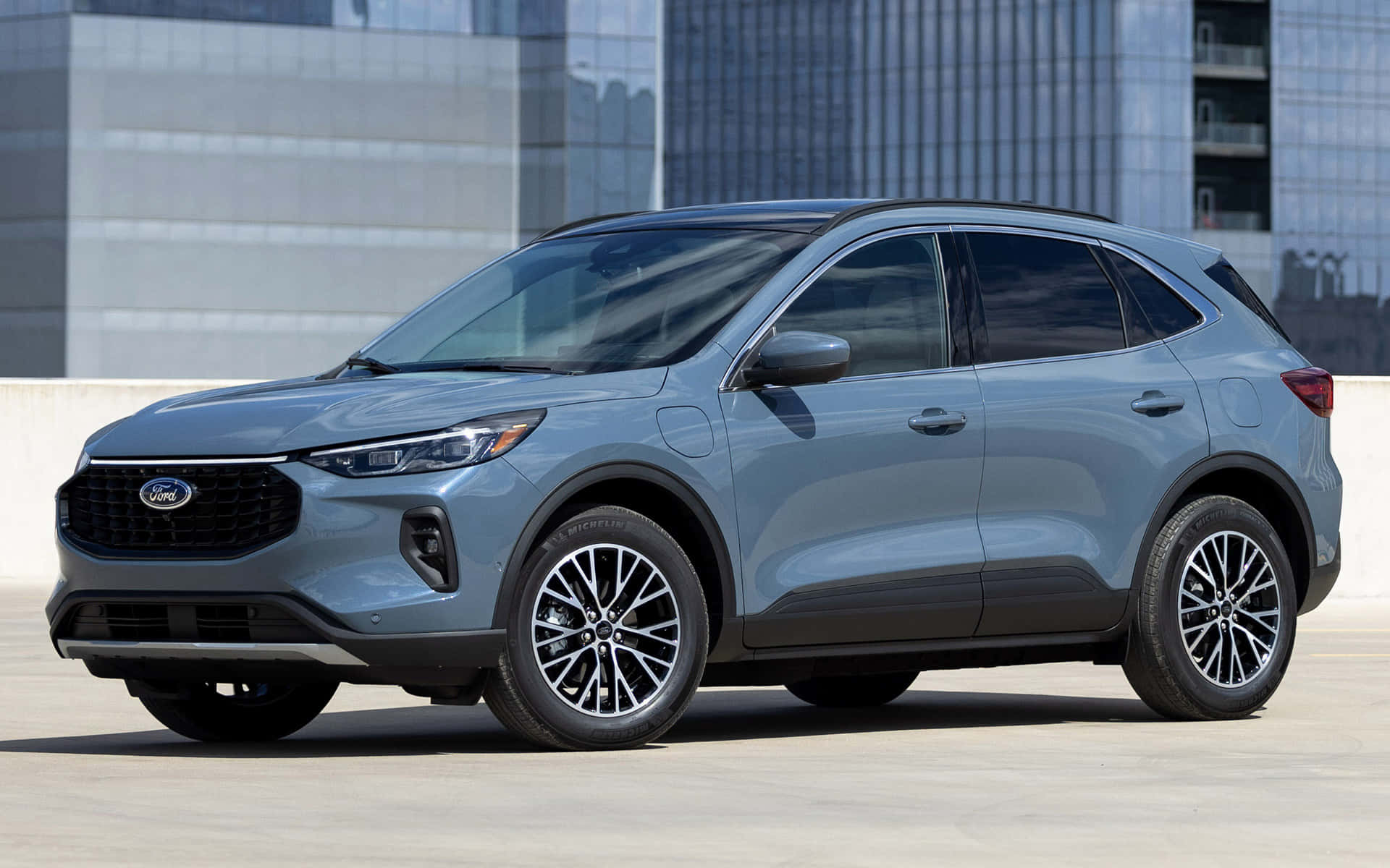 Ford Escape 桌布 壁紙 — 一架時尚的銀色福特電動SUV停放在混凝土廣場上，背景是現代玻璃摩天大樓。