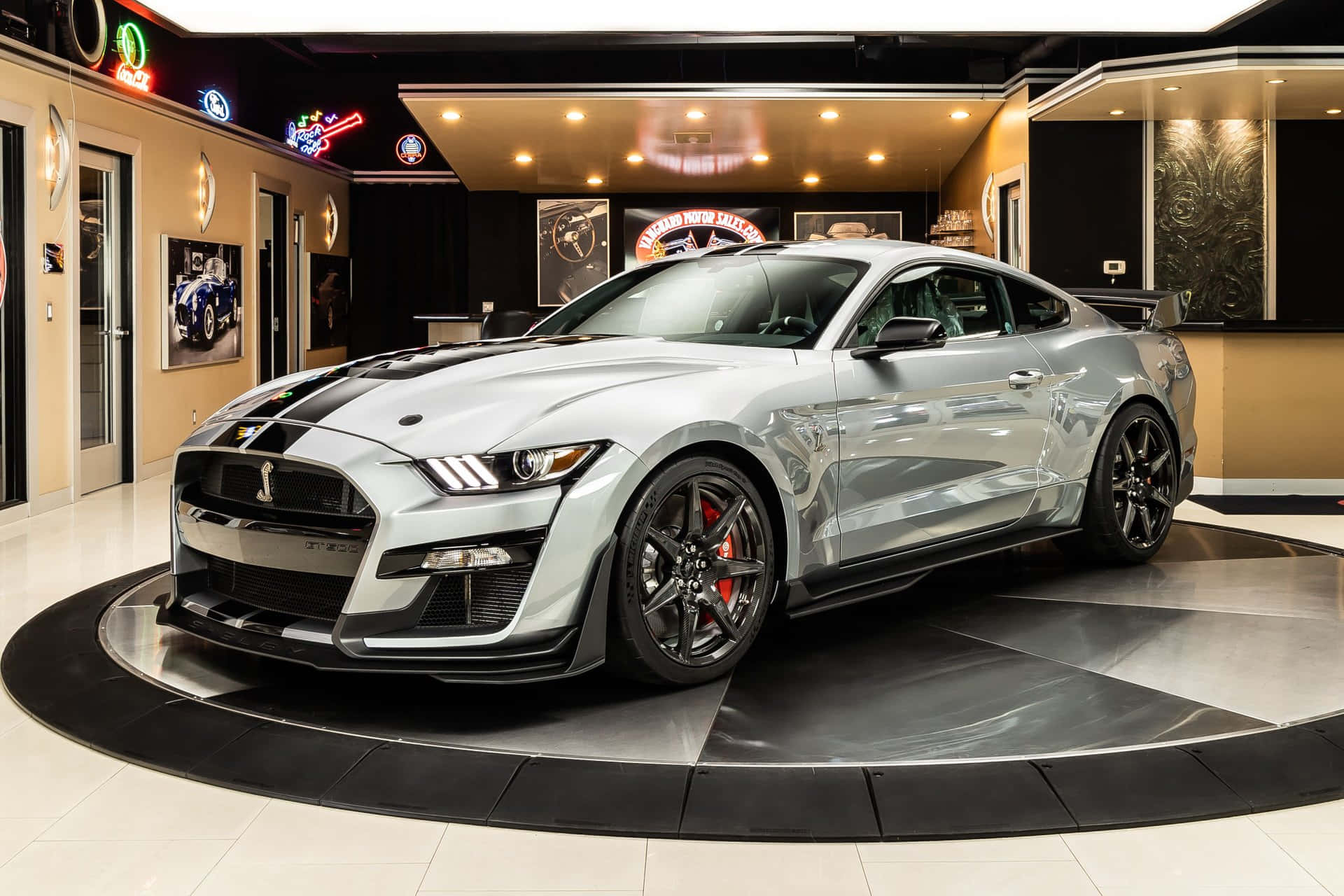  壁紙 — 一架時尚的銀色福特 Mustang GT 帶有黑色賽車條紋，位於現代汽車展廳的黑白棋盤格平台中央。
