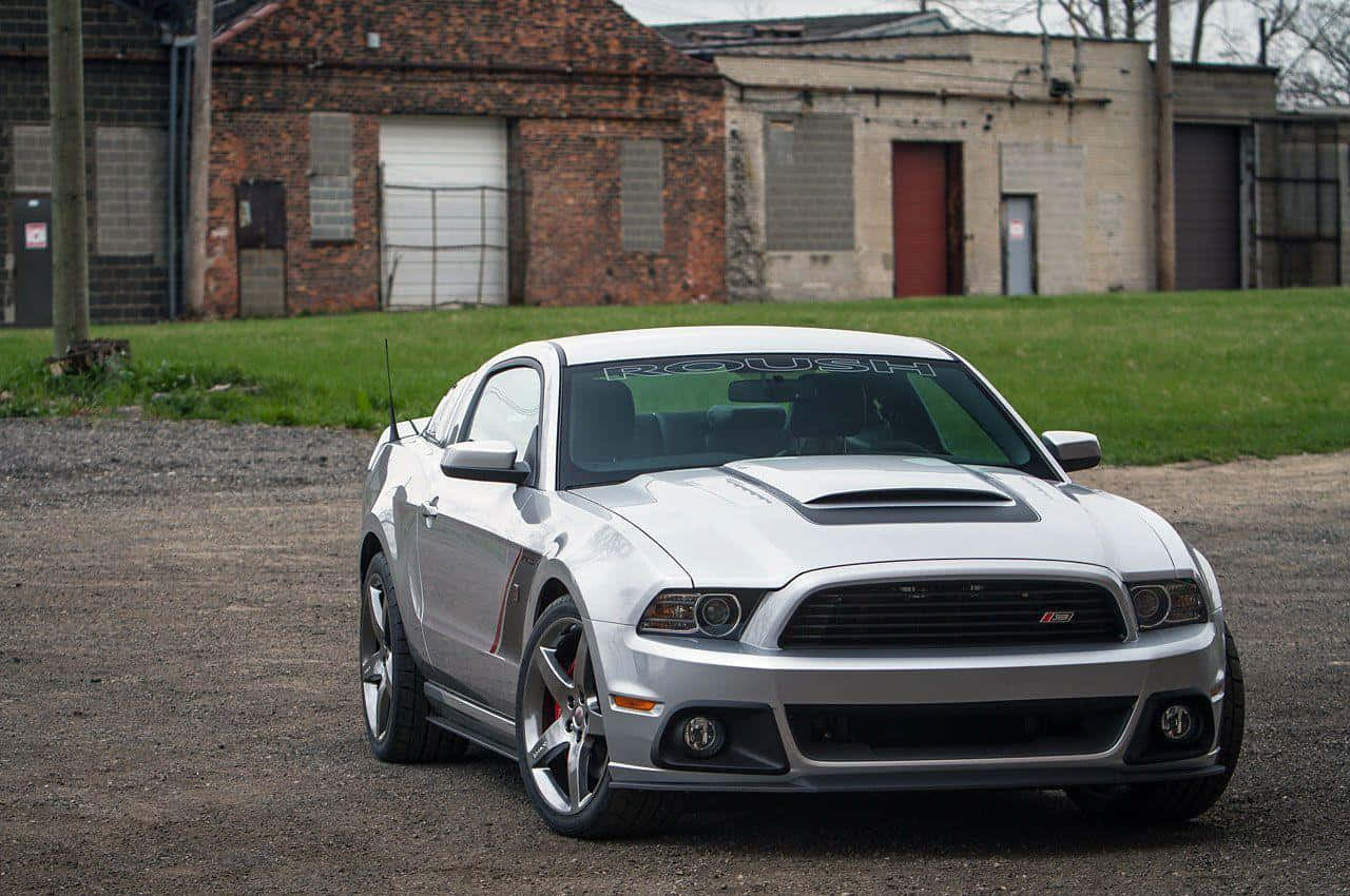 Ford Mustang Roush 桌布 壁紙 — 一架時尚的銀色福特野馬Shelby GT500停泊在碎石上，前方是風化的磚砌工業建築。