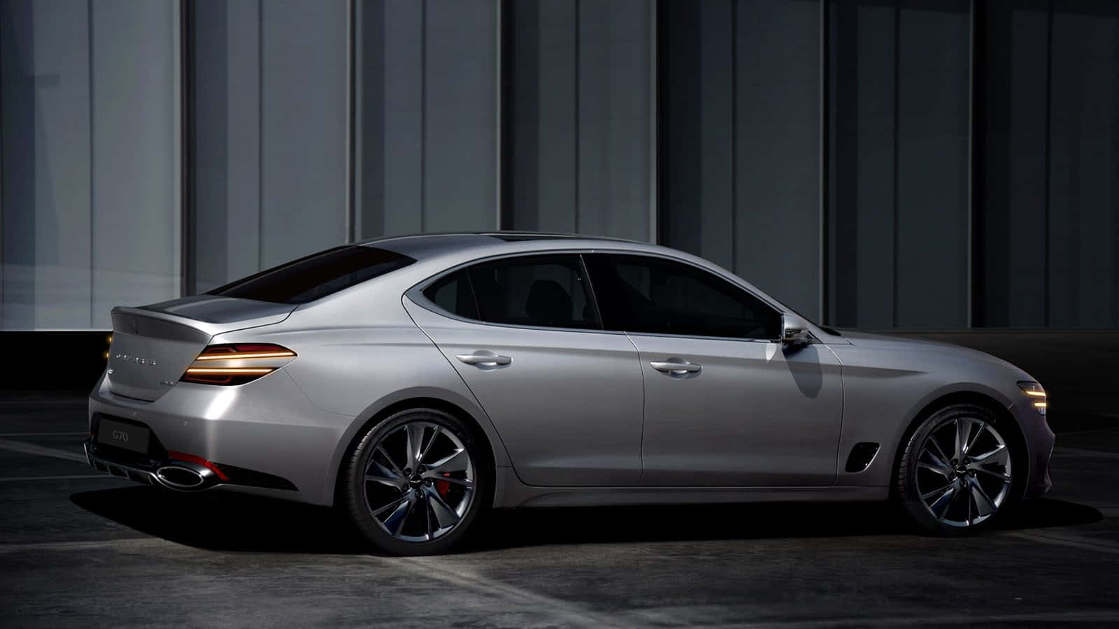 Genesis G70 桌布 壁紙 — 一輛時尚的銀色 Genesis G70 運動轎車在攝影棚燈光下，以深色垂直鑲板牆為背景閃閃發光。