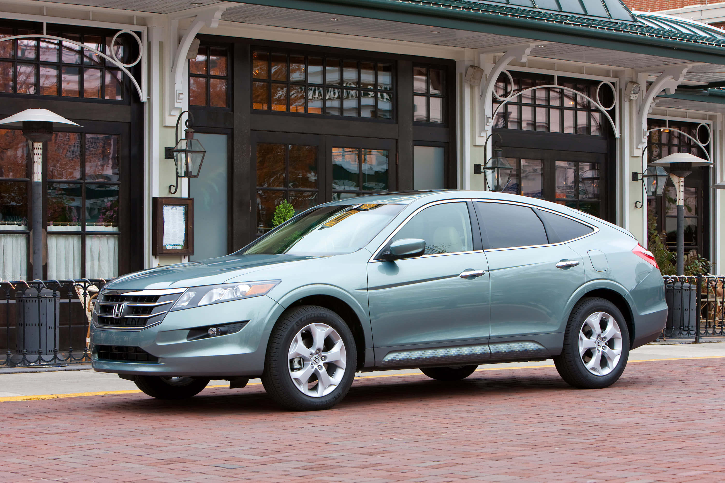 Honda Crosstour 桌布 壁紙 — 一輛時尚的銀色本田 Crosstour 停在紅磚街上，前面是經典的店面，有拱形窗戶和復古燈籠。