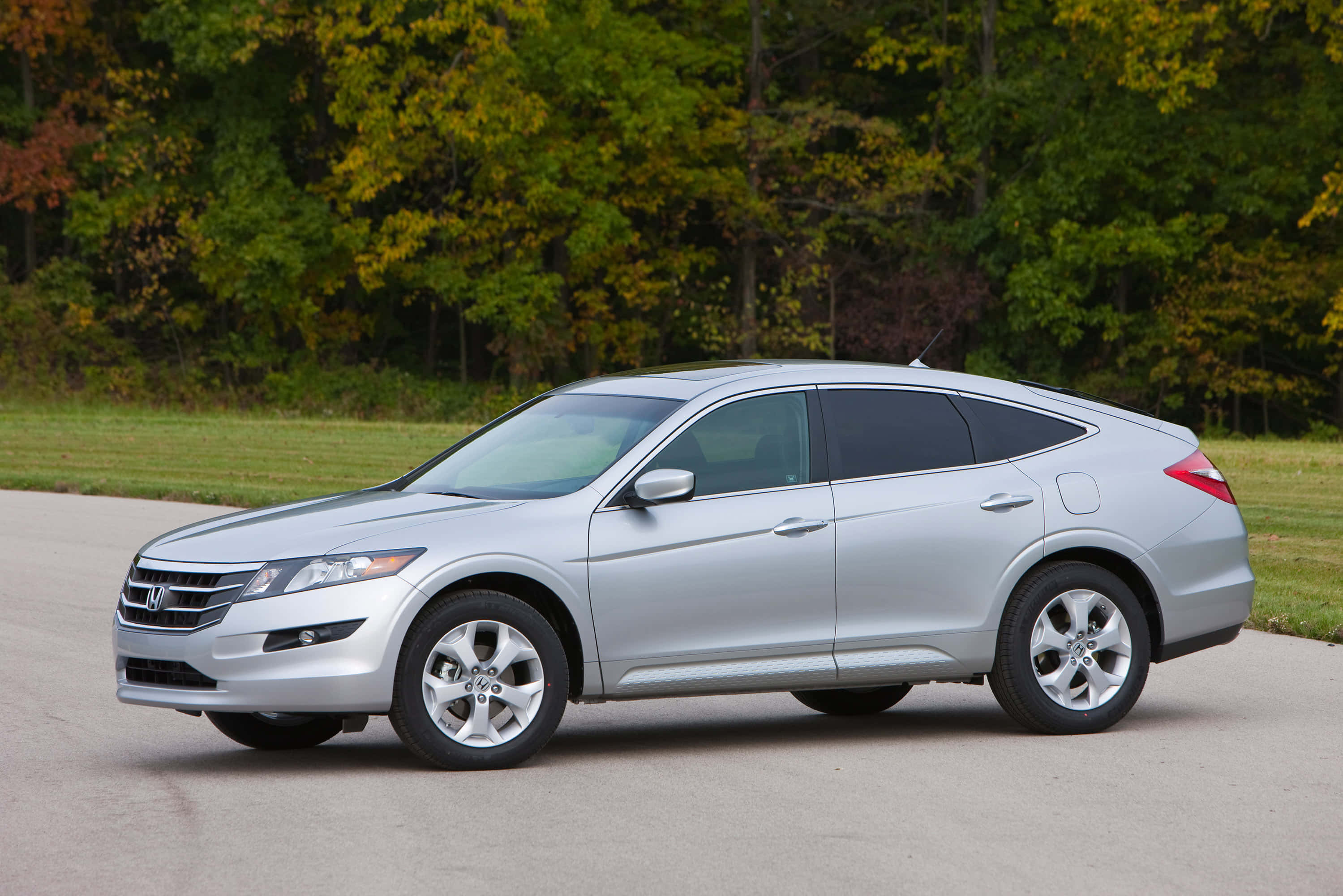Honda Crosstour 桌布 壁紙 — 一輛時尚的銀色本田 Crosstour SUV 停放在鋪砌道路上，背景有秋天的樹木。