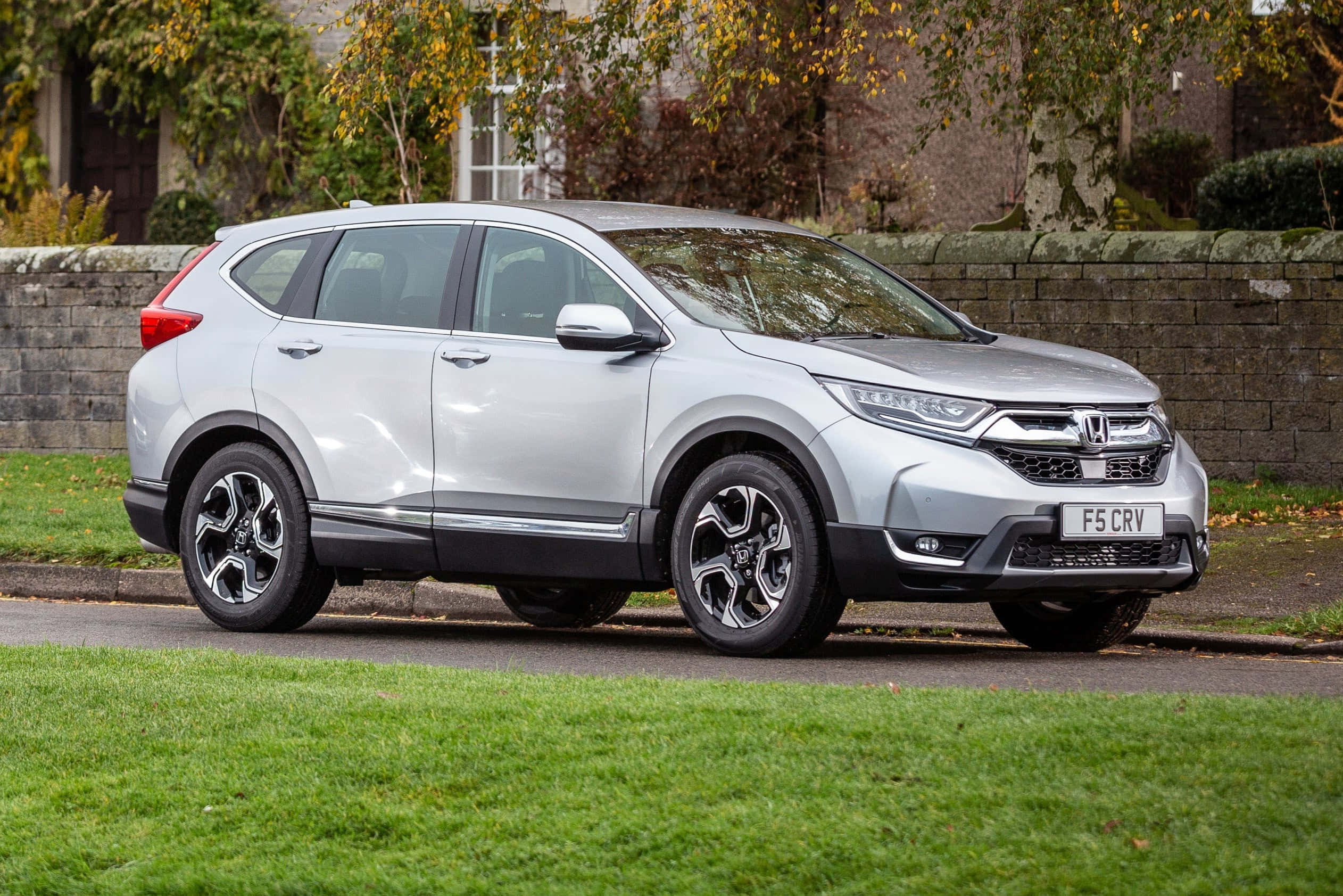 Honda Cr-v 桌布 壁紙 — 一輛時尚的銀色本田CRV SUV停在寧靜住宅區的街道旁，旁邊有石牆和秋樹。