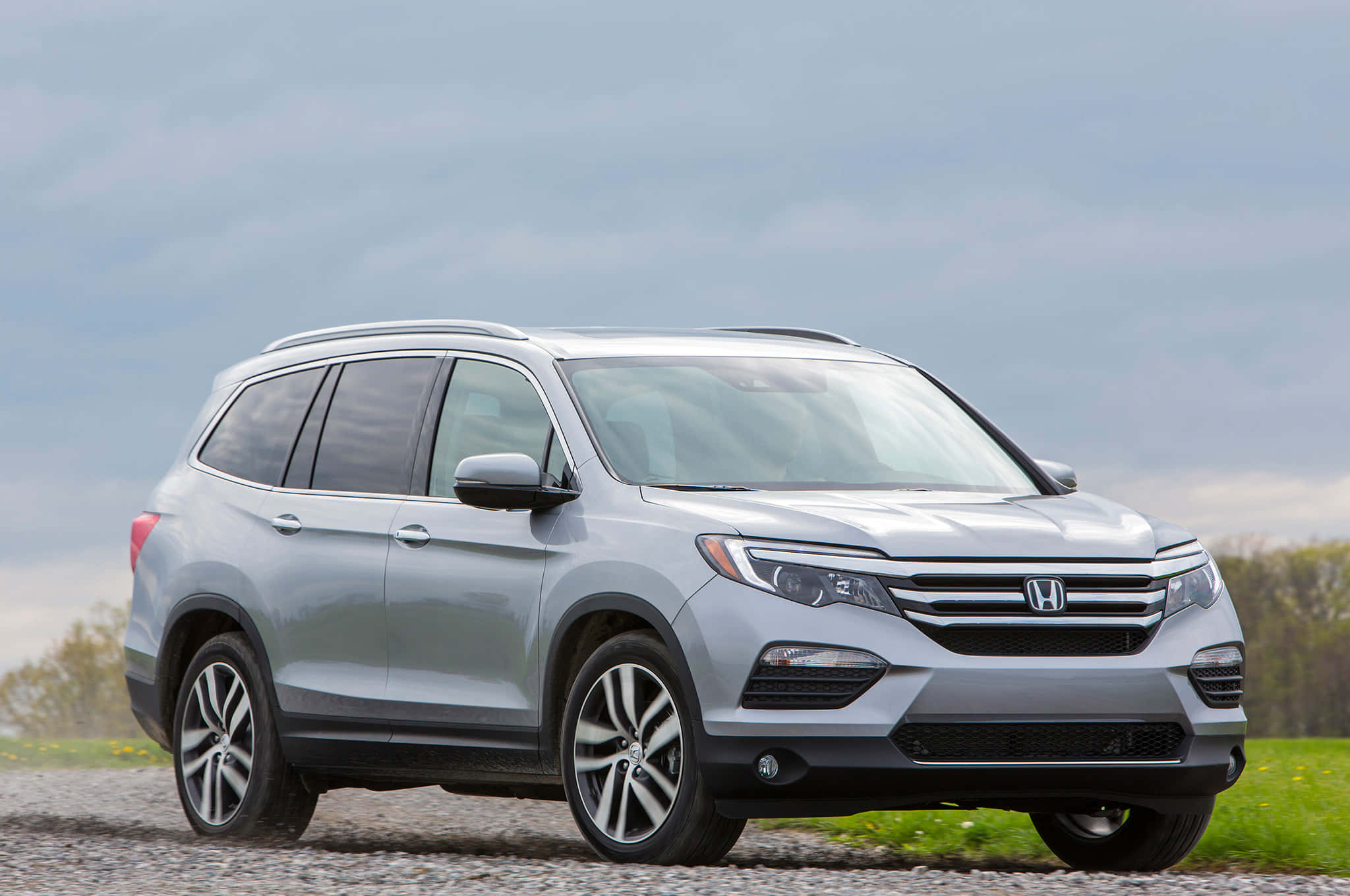 Honda Pilot 桌布 壁紙 — 一輛時尚的銀色本田Pilot SUV停放在碎石路上，背景有綠草和陰天。