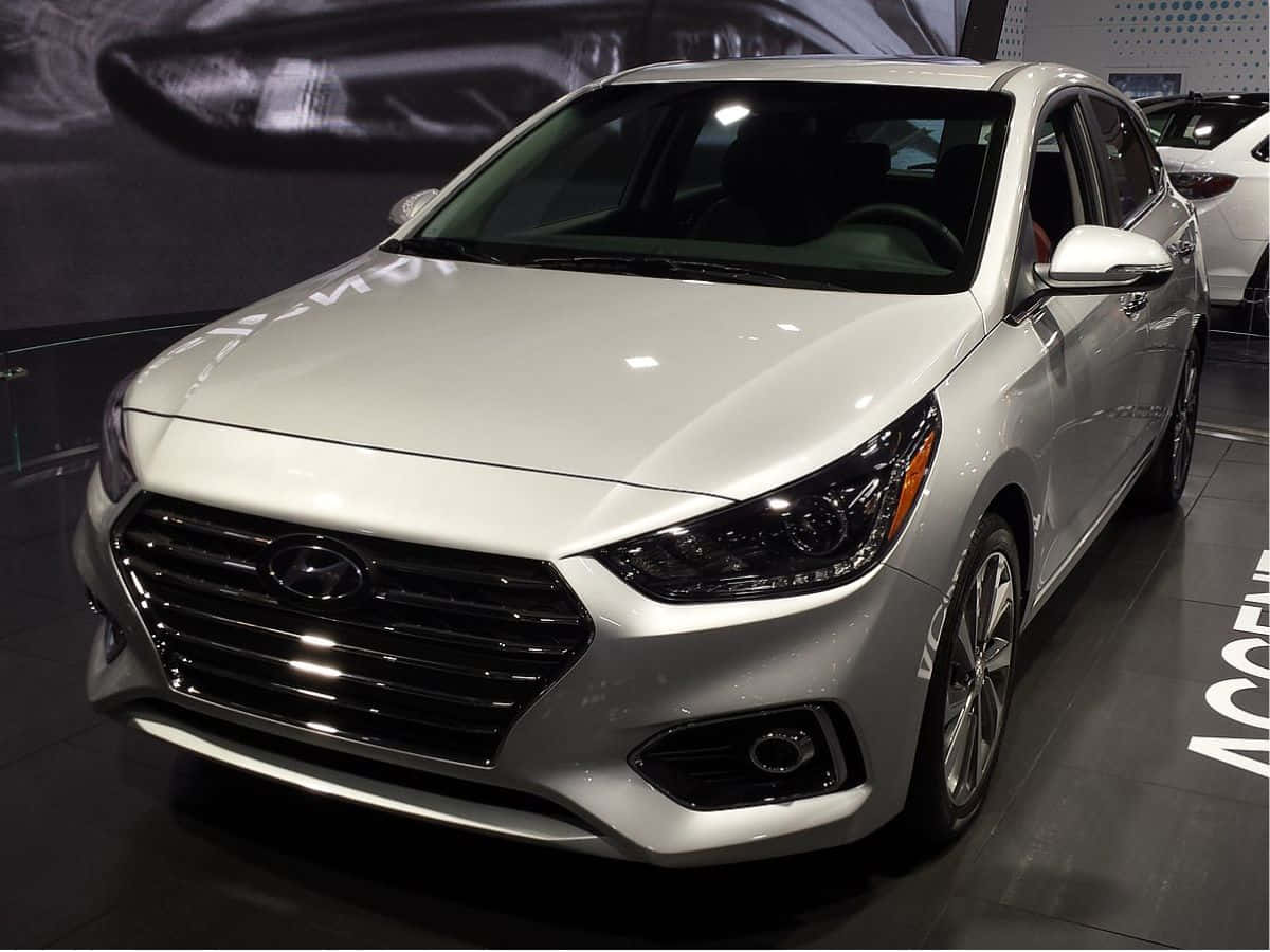 Hyundai Accent 桌布 壁紙 — 一輛時尚的銀色現代雅尊轎車在明亮的展廳燈光下閃耀，具有拋光飾面和現代格柵設計。