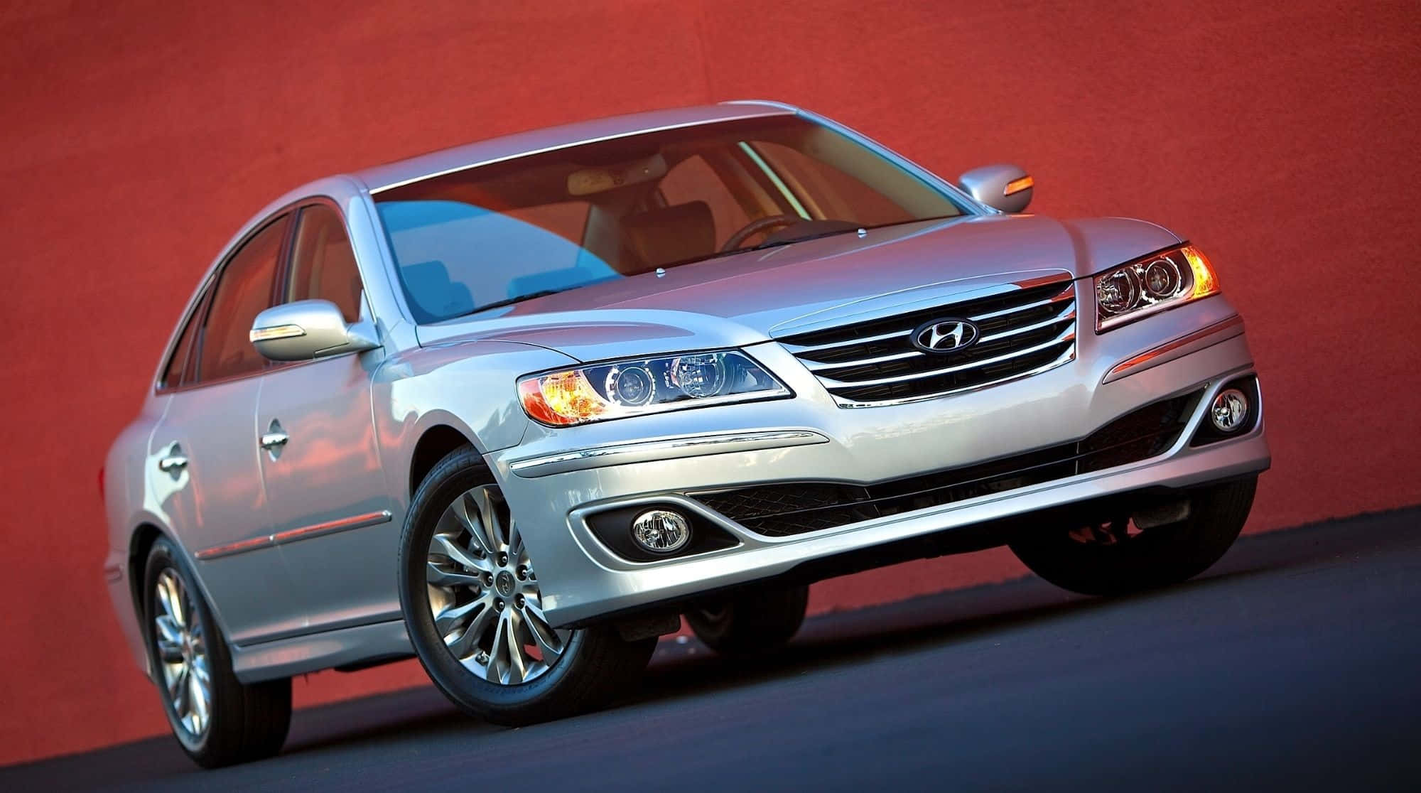 Hyundai Azera 桌布 壁紙 — 一輛時尚的銀色現代轎車在攝影棚燈光下，映襯著鮮紅色的牆壁閃閃發光。