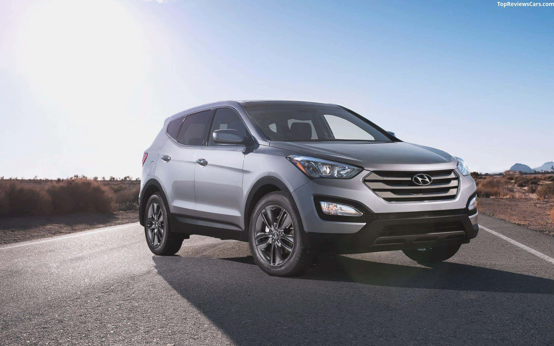 Hyundai Santa Fe 桌布 壁紙 — 一輛時尚的銀色現代SUV在陽光明媚的沙漠公路上自信行駛，遠山在清澈的藍天下清晰可見。