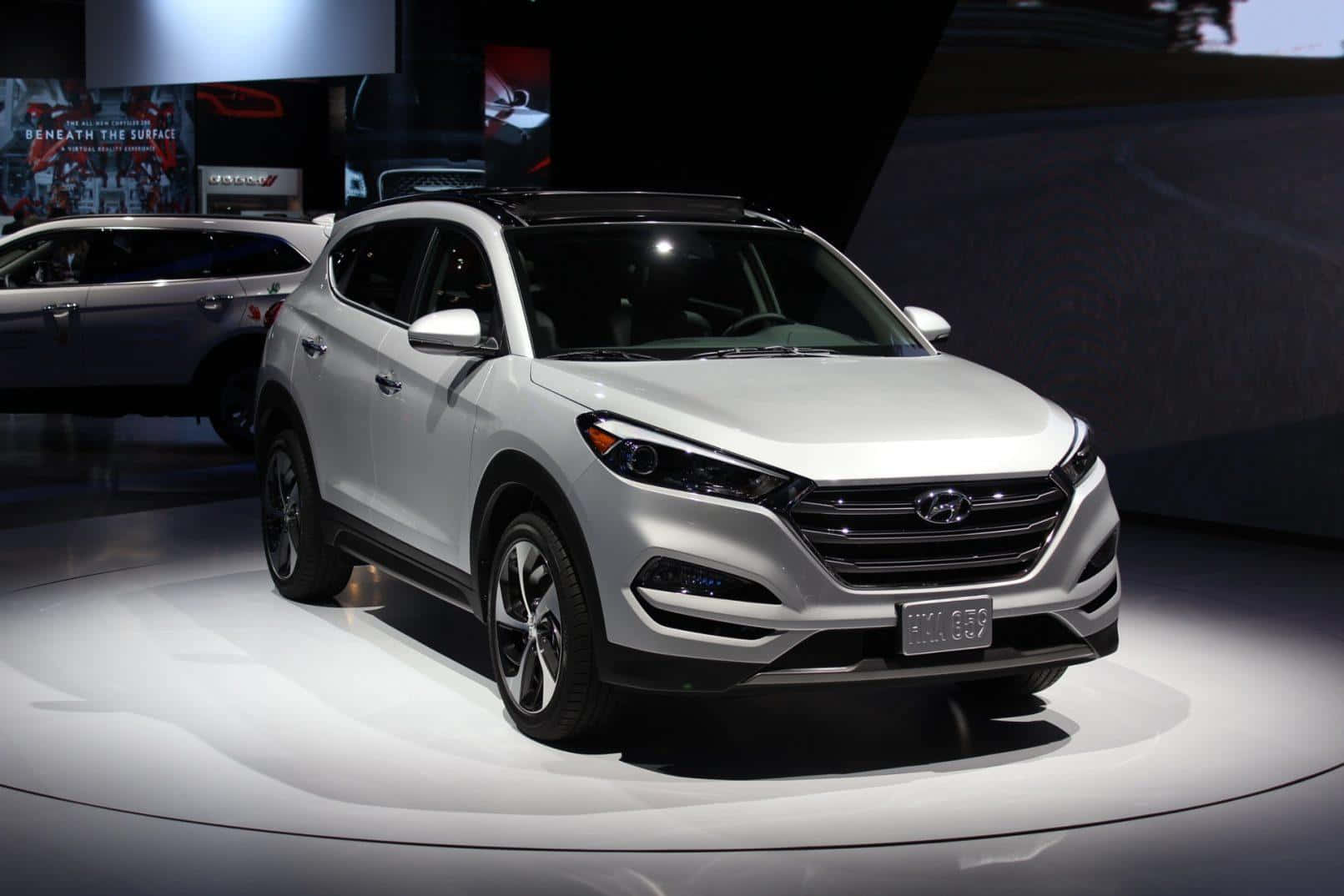 Hyundai Tucson 桌布 壁紙 — 一輛時尚的銀色現代 Tucson SUV 在車展的明亮圓形平台上，在戲劇性的聚光燈下展示。