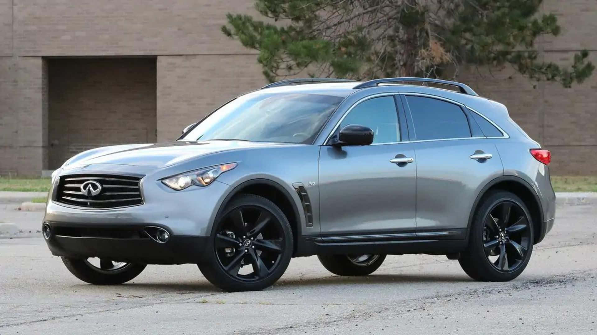 Infiniti Qx70 桌布 壁紙 — 一輛時尚的銀色Infiniti QX70 SUV，配備黑色輪圈，停在磚造建築前的瀝青路面上，周圍有樹木。