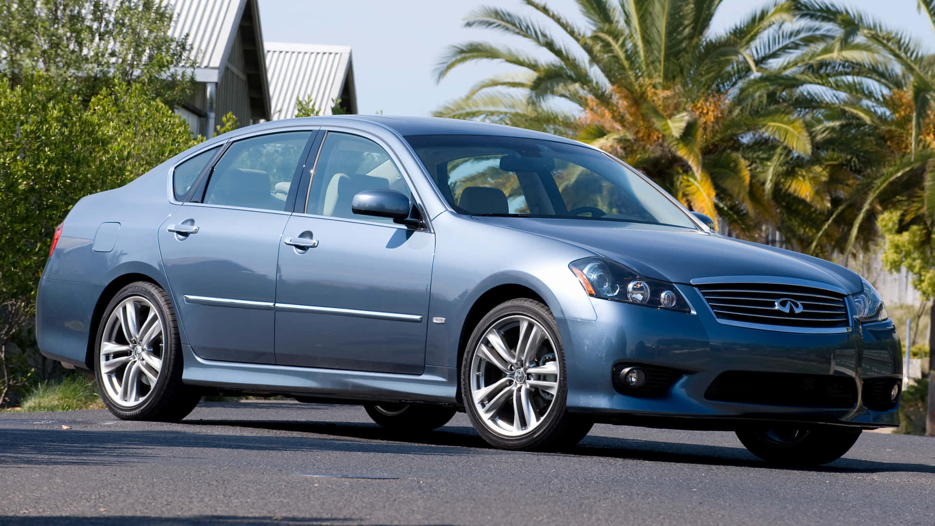 Infiniti M35 桌布 壁紙 — 一輛時尚的銀色Infiniti轎車停在柏油路上，背景有棕櫚樹和房屋，在明亮的日光下。