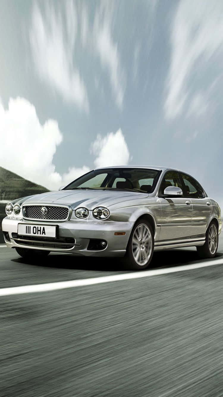 Jaguar X-type 桌布 壁紙 — 一輛時尚的銀色積架房車沿著蜿蜒的道路疾馳，背景中的雲朵和山丘因動態模糊而變得朦朧。