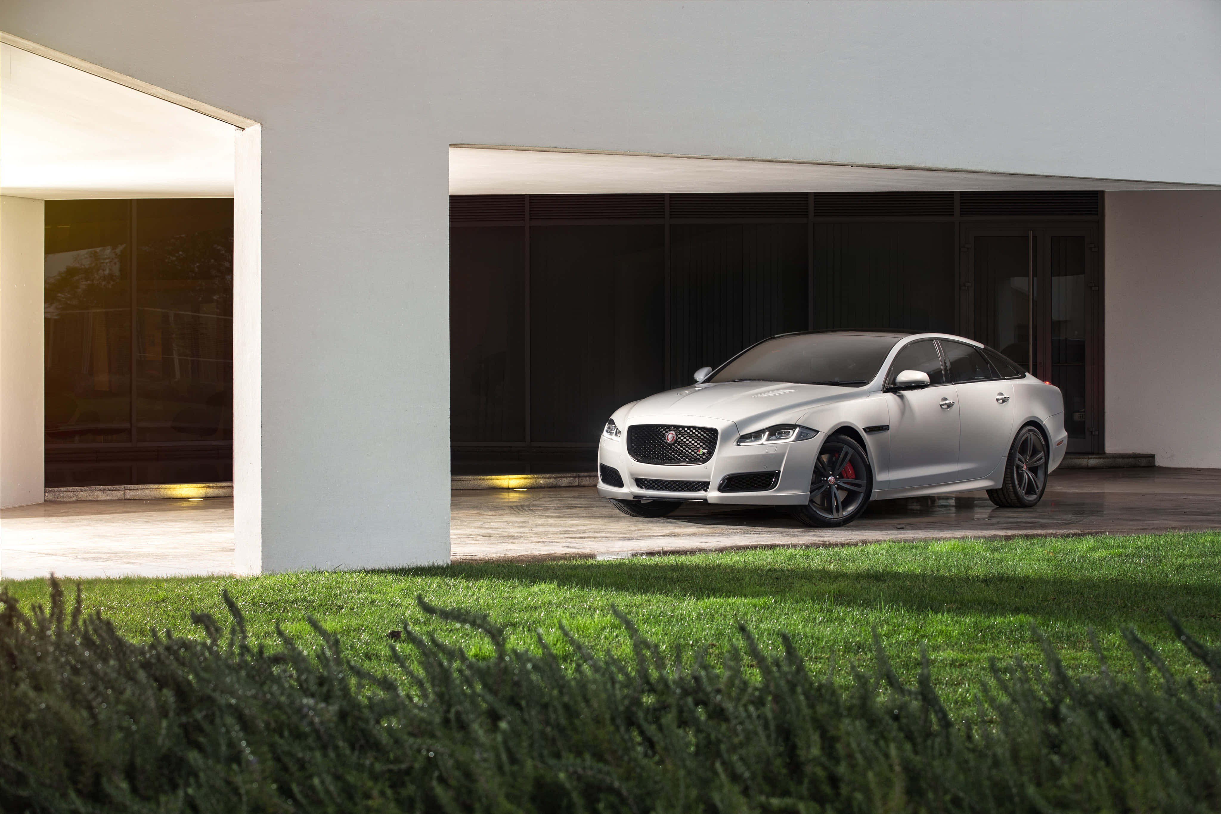 Jaguar Xjr 桌布 壁紙 — 一輛時尚的銀色捷豹XF停放在現代白色房屋下，房屋有玻璃門和前景的綠色草地。