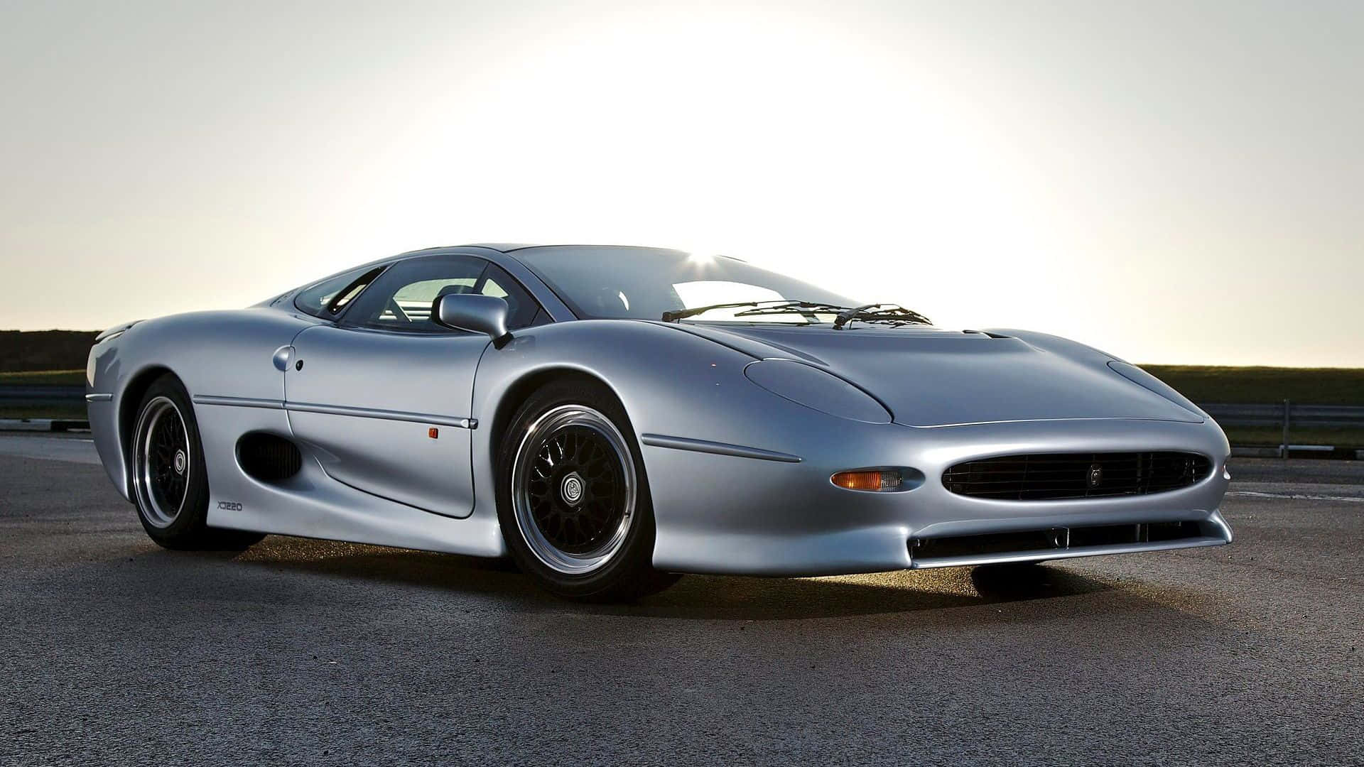 Jaguar Xj220 桌布 壁紙 — 一輛時尚的銀色積架XJ220跑車在開闊的高速公路上，在金色夕陽下閃閃發光。