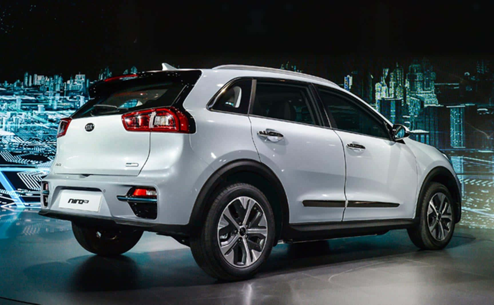 Kia Niro 桌布 壁紙 — 一部時尚的銀色Kia Niro SUV在閃亮舞台上展示，背景是發光的藍色城市景觀。