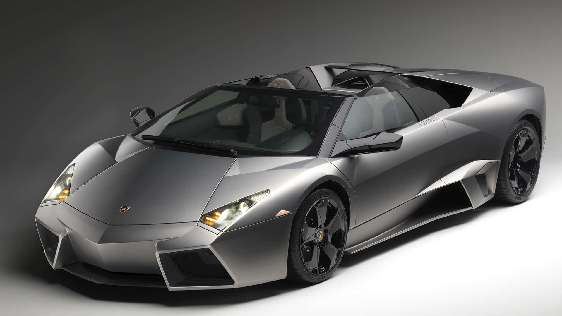 Lamborghini Reventón 桌布 壁紙 — 一部時尚的銀色藍寶堅尼 Reventon Roadster，帶有黑色飾邊和發光的車頭燈，在簡約的灰色工作室背景下擺拍。