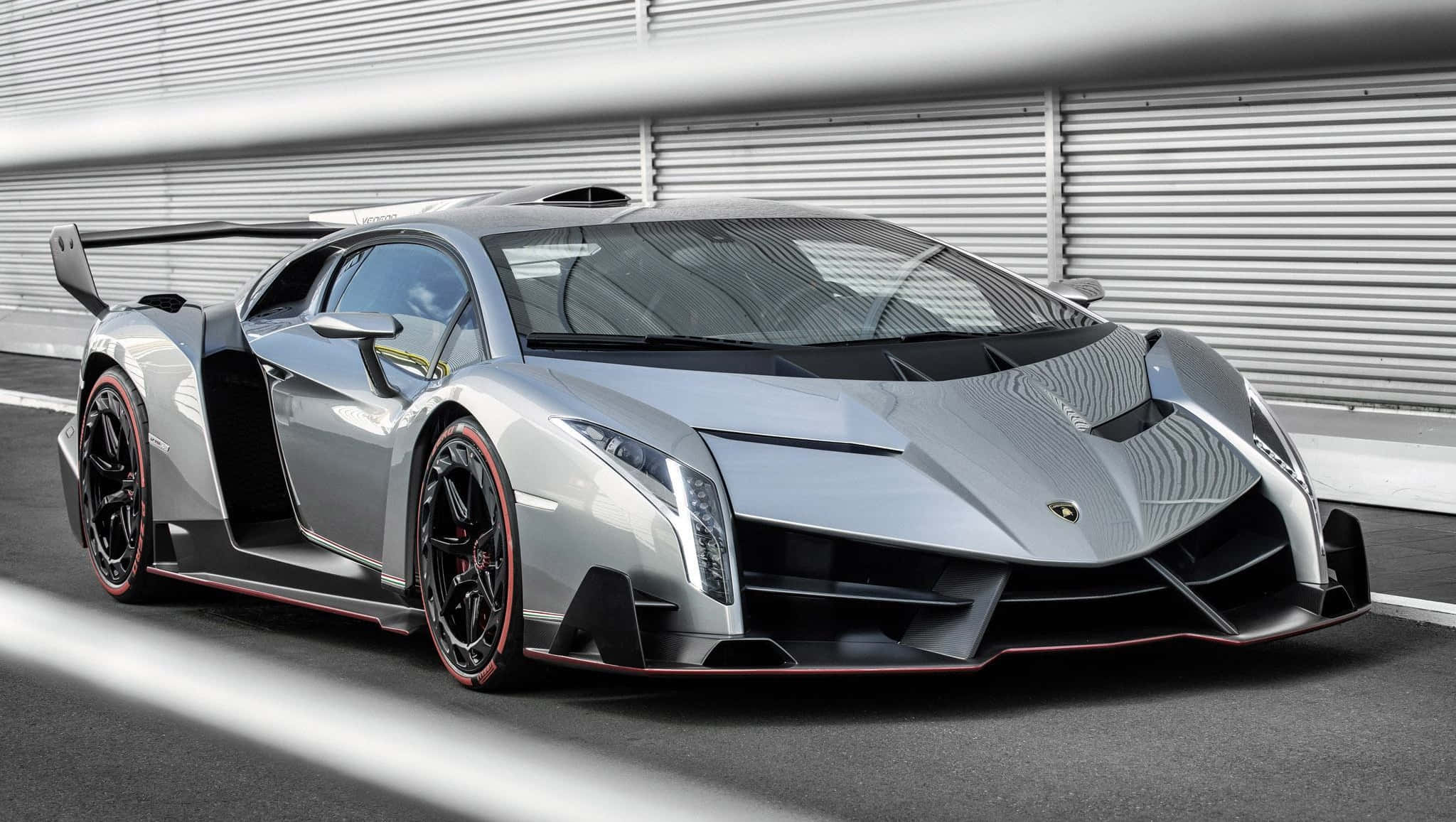 Lamborghini Veneno 桌布 壁紙 — 一輛時尚的銀色藍寶堅尼 Veneno 帶有紅色點綴，停泊在賽車場上，背景是波紋金屬牆。