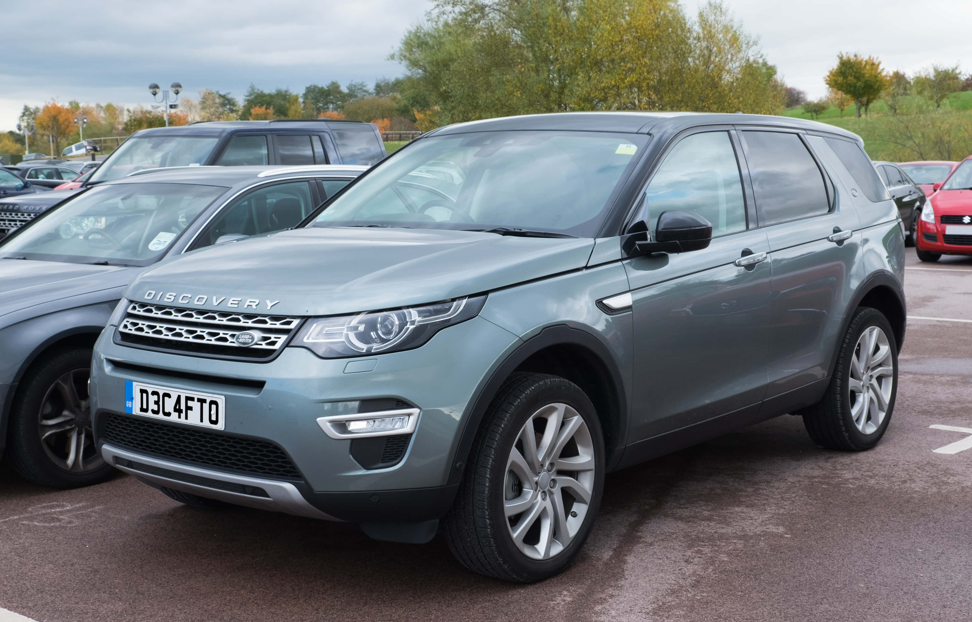 Land Rover Discovery 桌布 壁紙 — 一輛時尚的銀色 Land Rover Discovery SUV 停放在停車場，背景有秋樹和陰天。