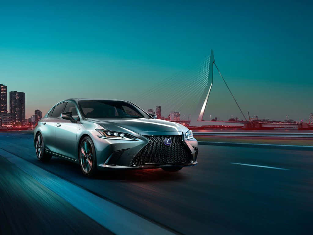 Lexus Es 300h 桌布 壁紙 — 一輛時尚的銀色Lexus轎車在黃昏時分沿著城市高速公路行駛，背景是現代橋樑和發光的天際線。