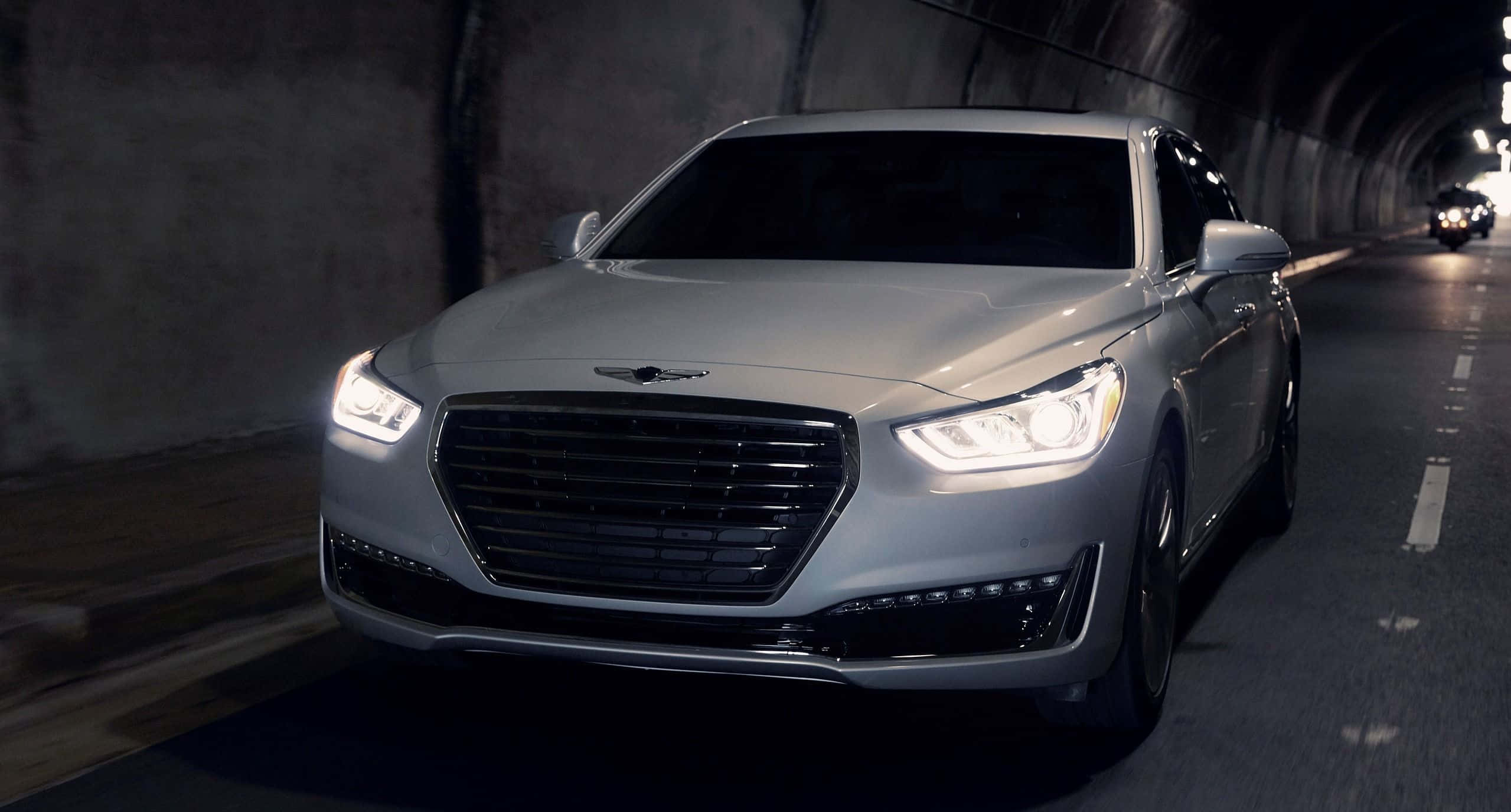 Hyundai Genesis 桌布 壁紙 — 一輛時尚的銀色豪華轎車在光線昏暗的混凝土隧道內亮著車頭燈向前行駛。