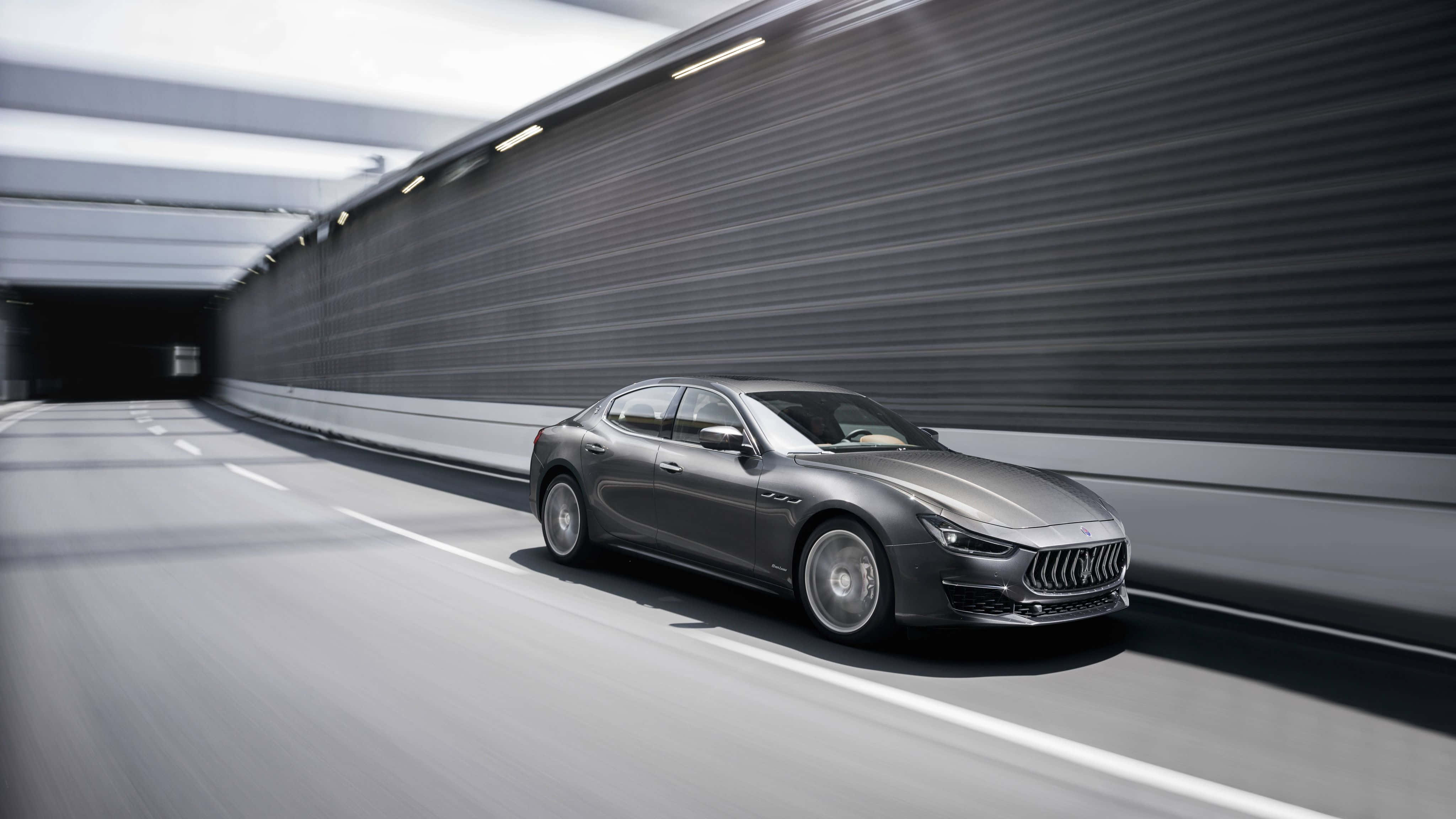 Maserati Ghibli 桌布 壁紙 — 一輛時尚的銀色瑪莎拉蒂跑車在現代隧道中疾馳，牆壁上呈現動態模糊效果。